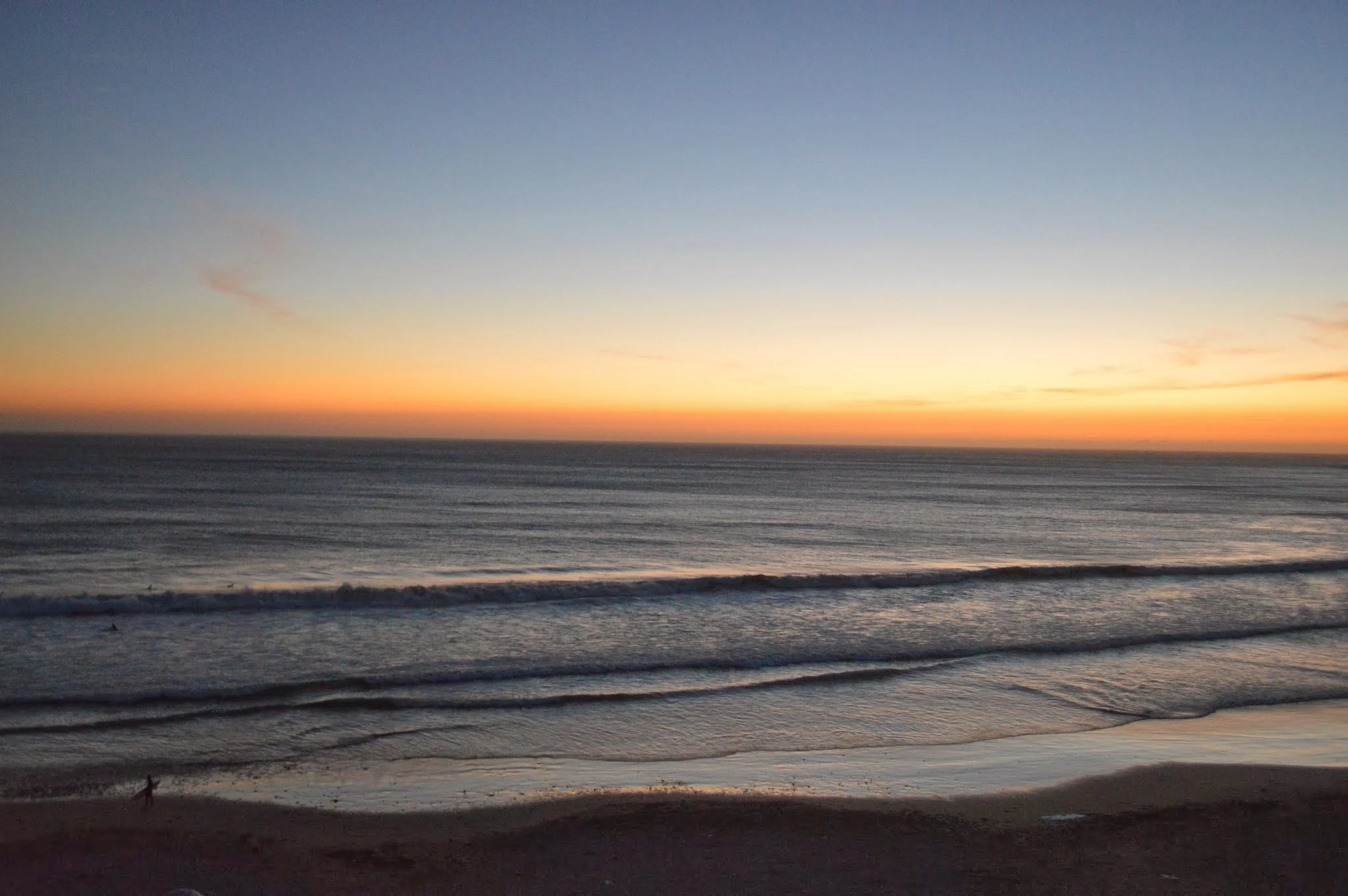 Sunset over the ocean with a colorful sky and waves on the beach.