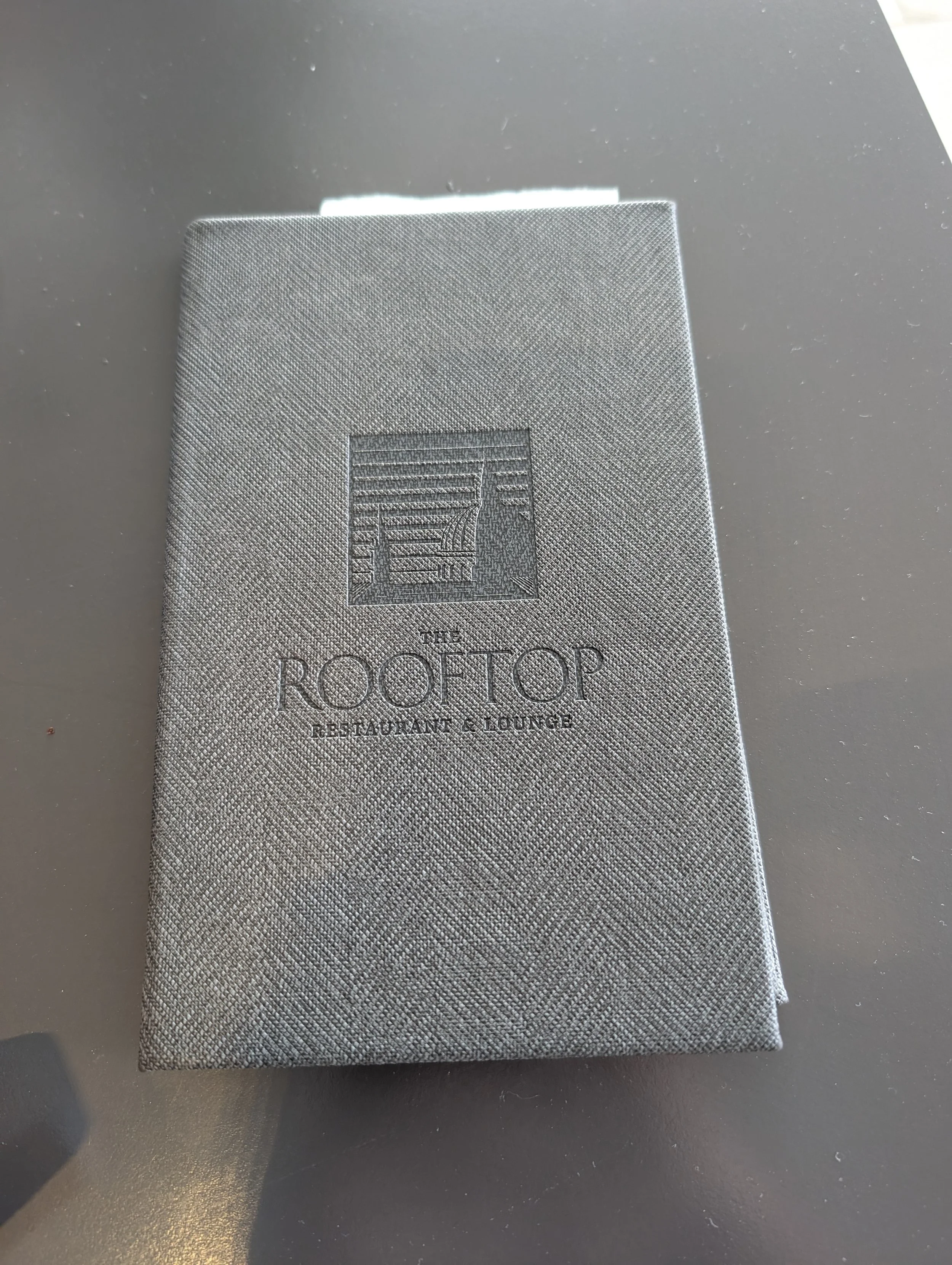 A textured silver card with the words 'The Rooftop Restaurant & Lounge' and an illustration of a building with a rooftop on it.