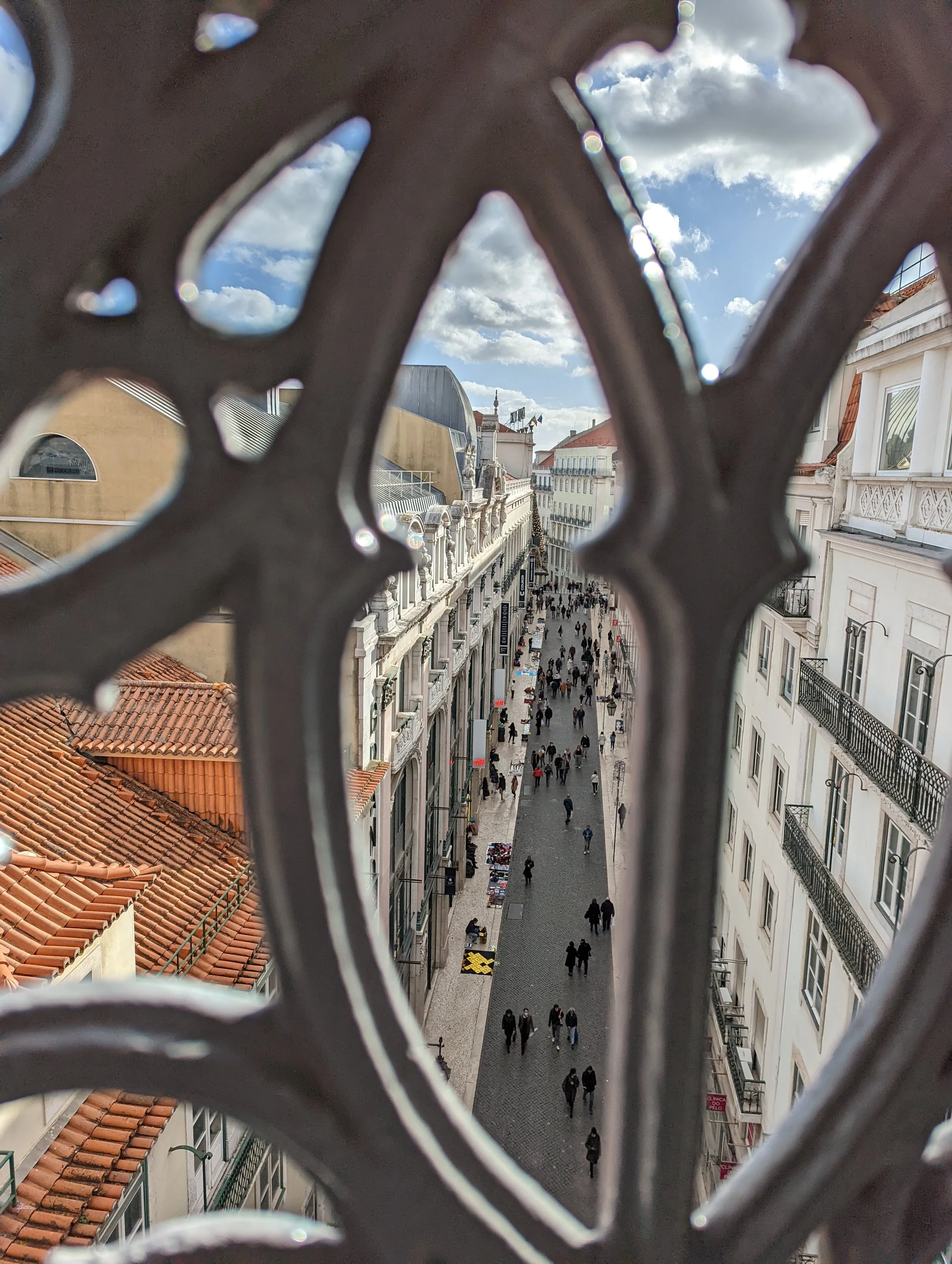 City street view seen through an ornamental metal fence with cloud-filled sky