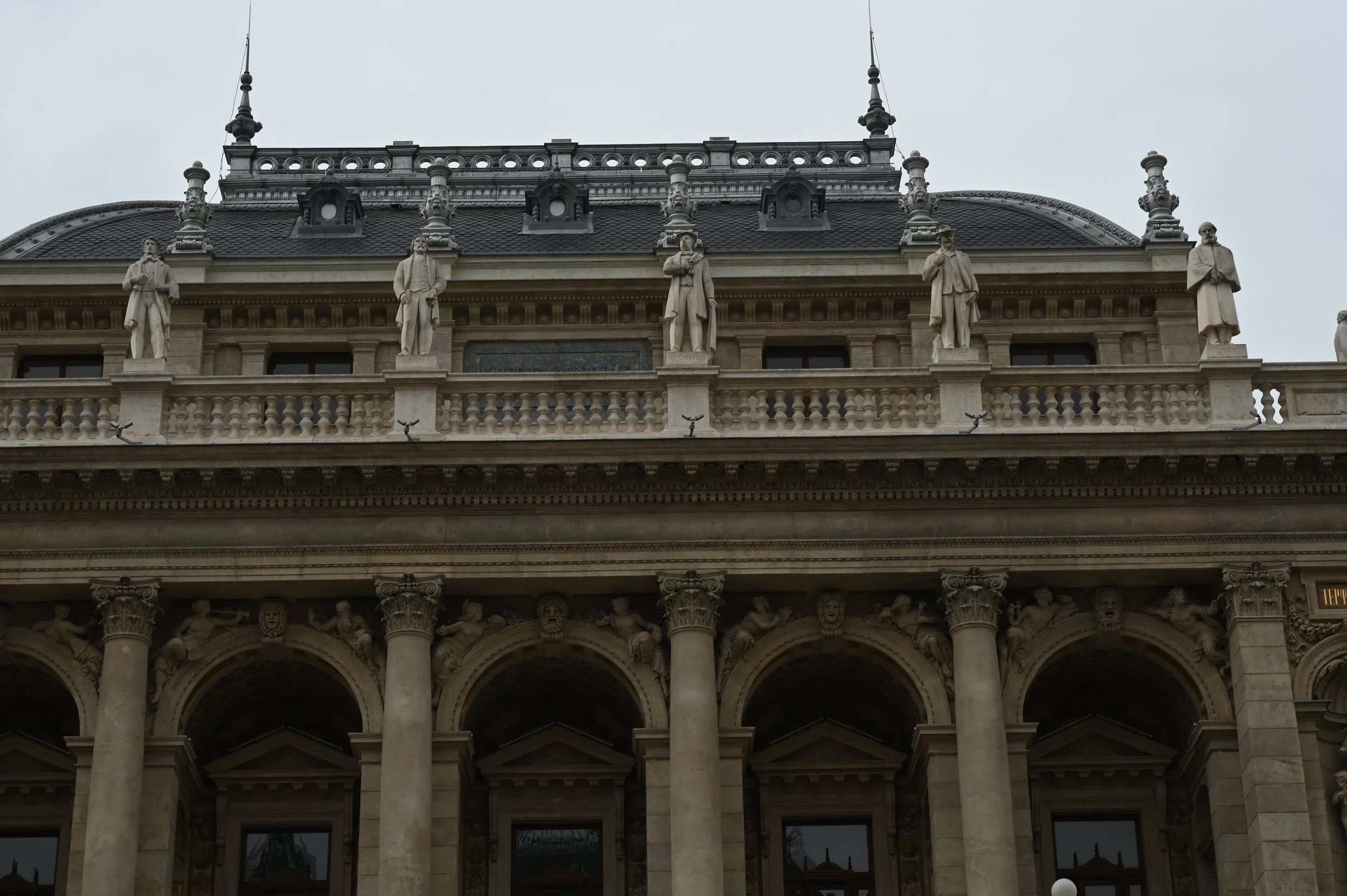 Close-up of the architectural details on the façade of a historic building, featuring statues of robed figures, Corinthian columns, and ornate stone carvings.