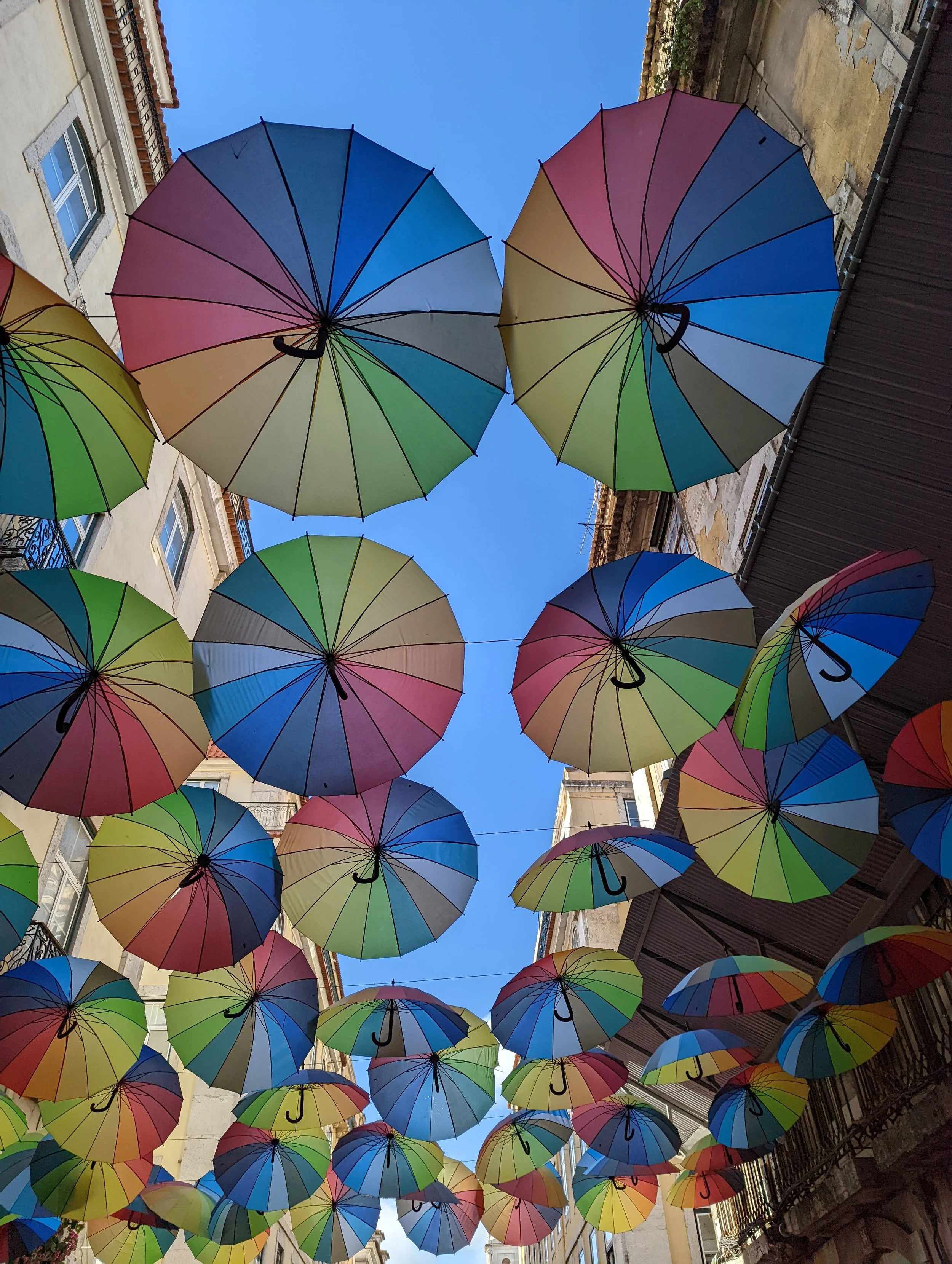 Colorful umbrellas hanging above a street, creating a canopy against a clear blue sky.