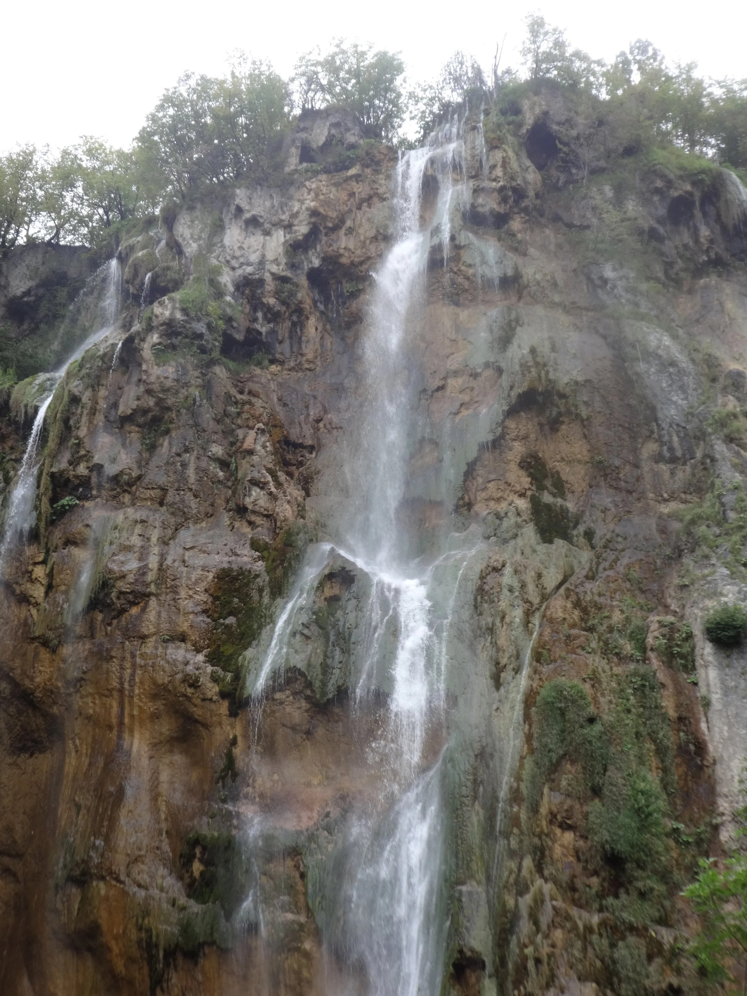 A waterfall cascading down a rocky cliff surrounded by green trees.