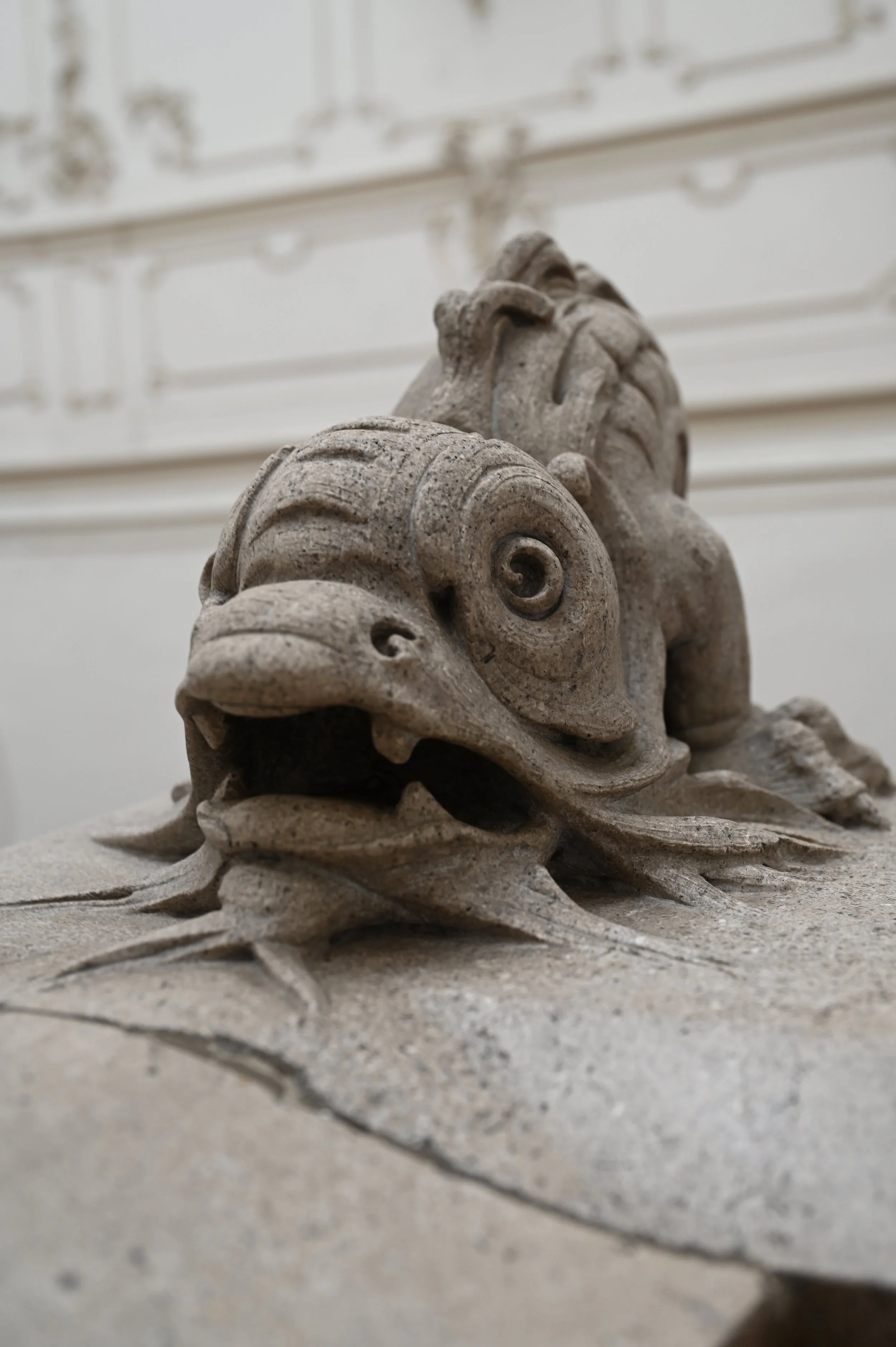 Close-up of a carved stone sculpture of a lion's head with a decorative mane, placed on a flat surface.