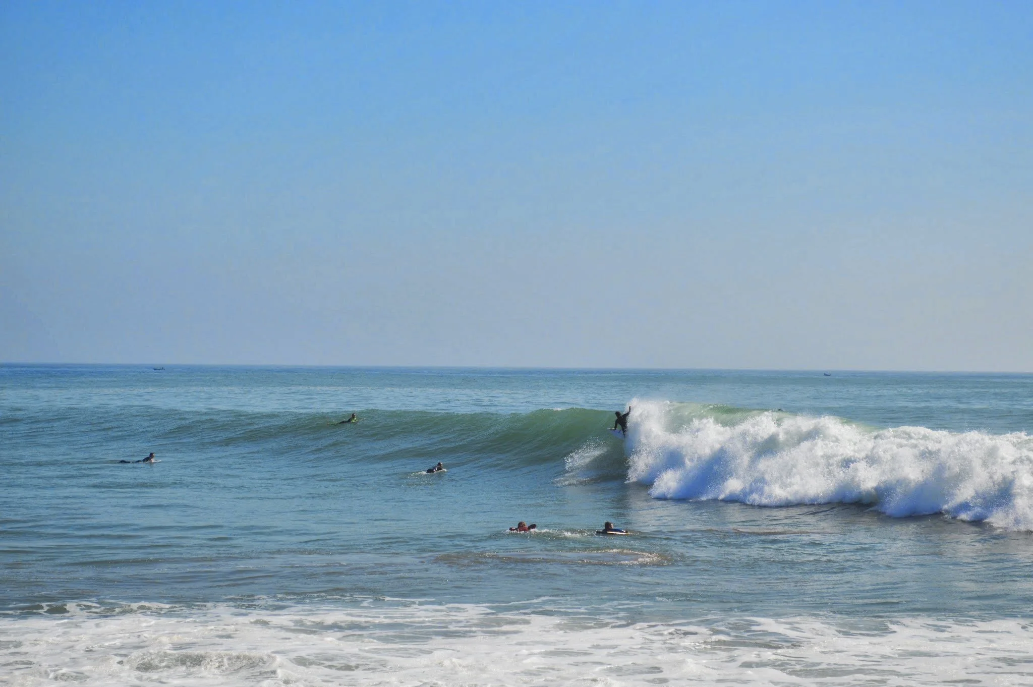 People enjoying surfing in the ocean with a clear blue sky and gentle waves.