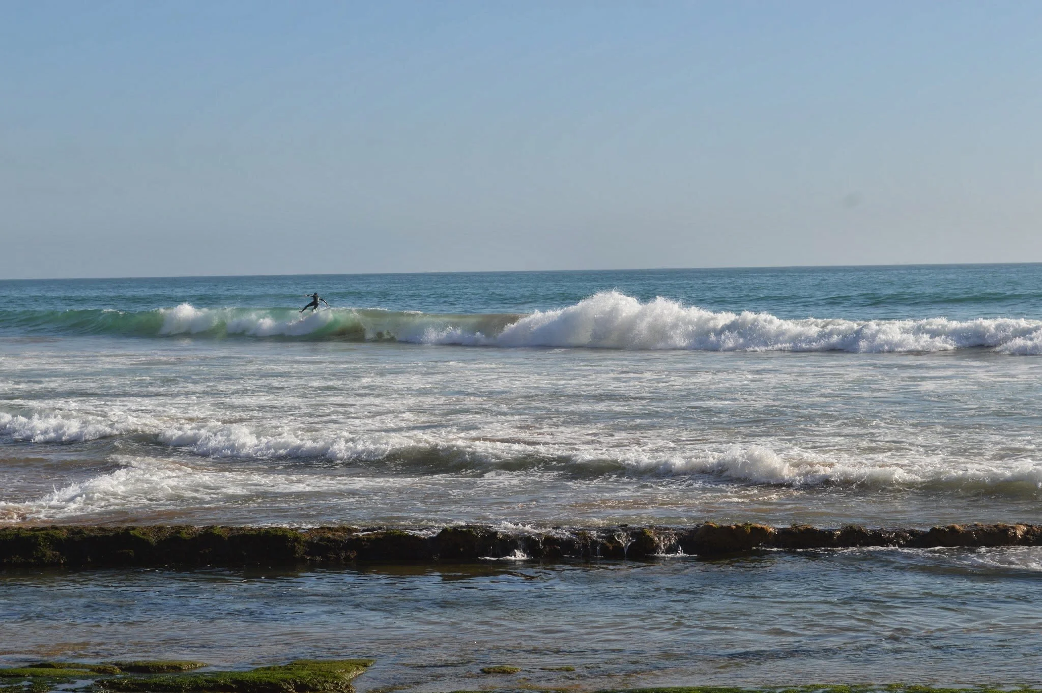A person surfing on a wave in the ocean under a clear, blue sky.