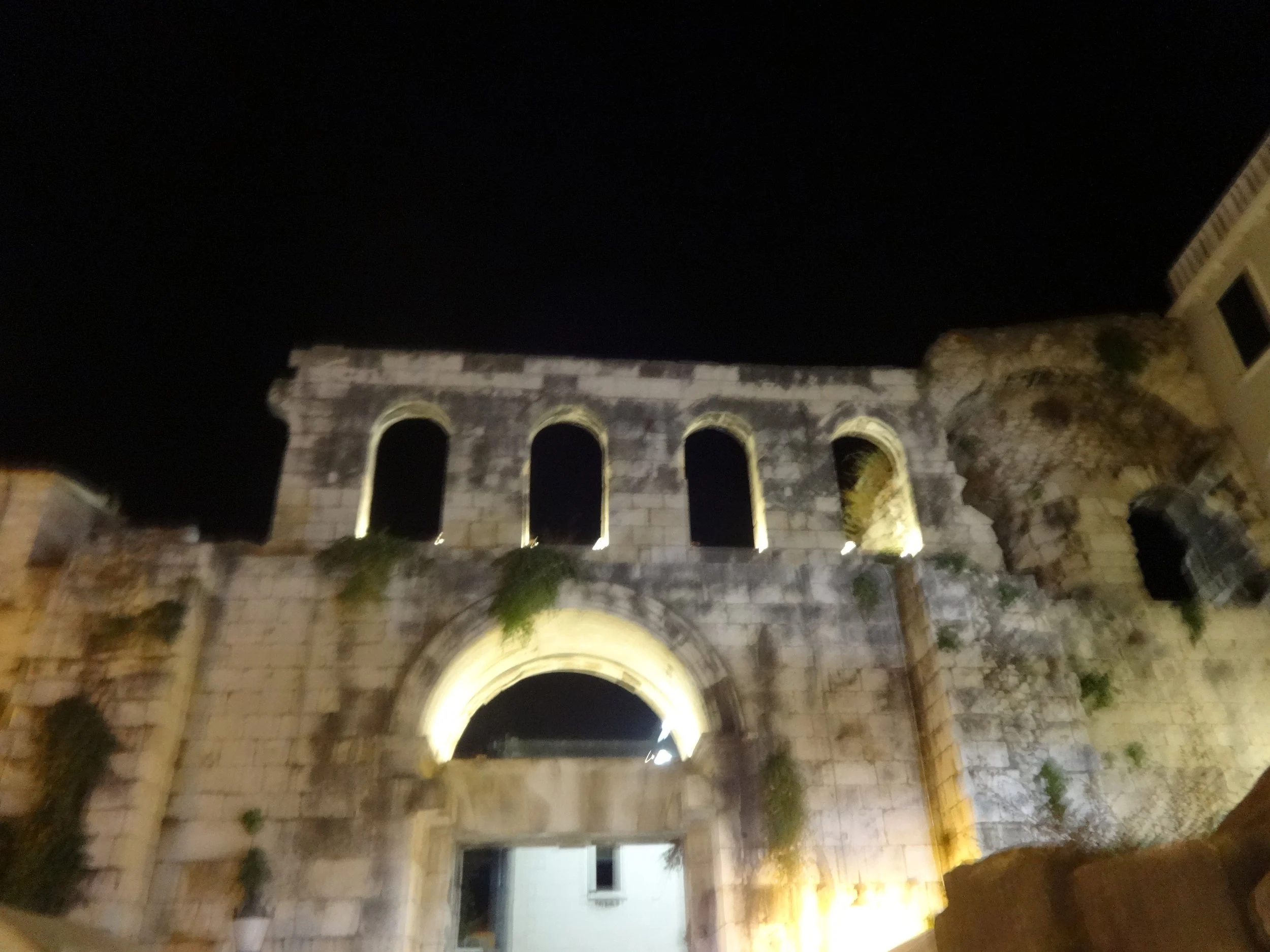Night view of ancient Roman aqueduct with arches illuminated, next to a modern building with lit windows.