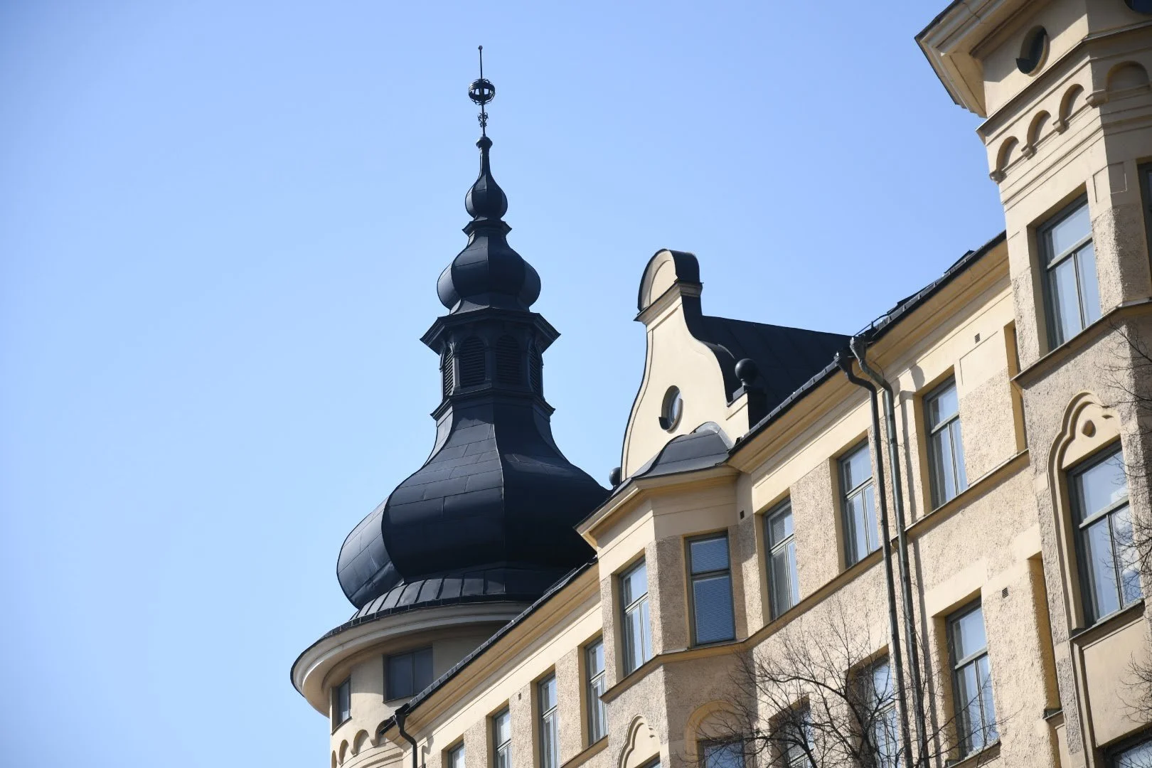 Building with ornate architecture and a tall, decorative black spire against a clear blue sky.