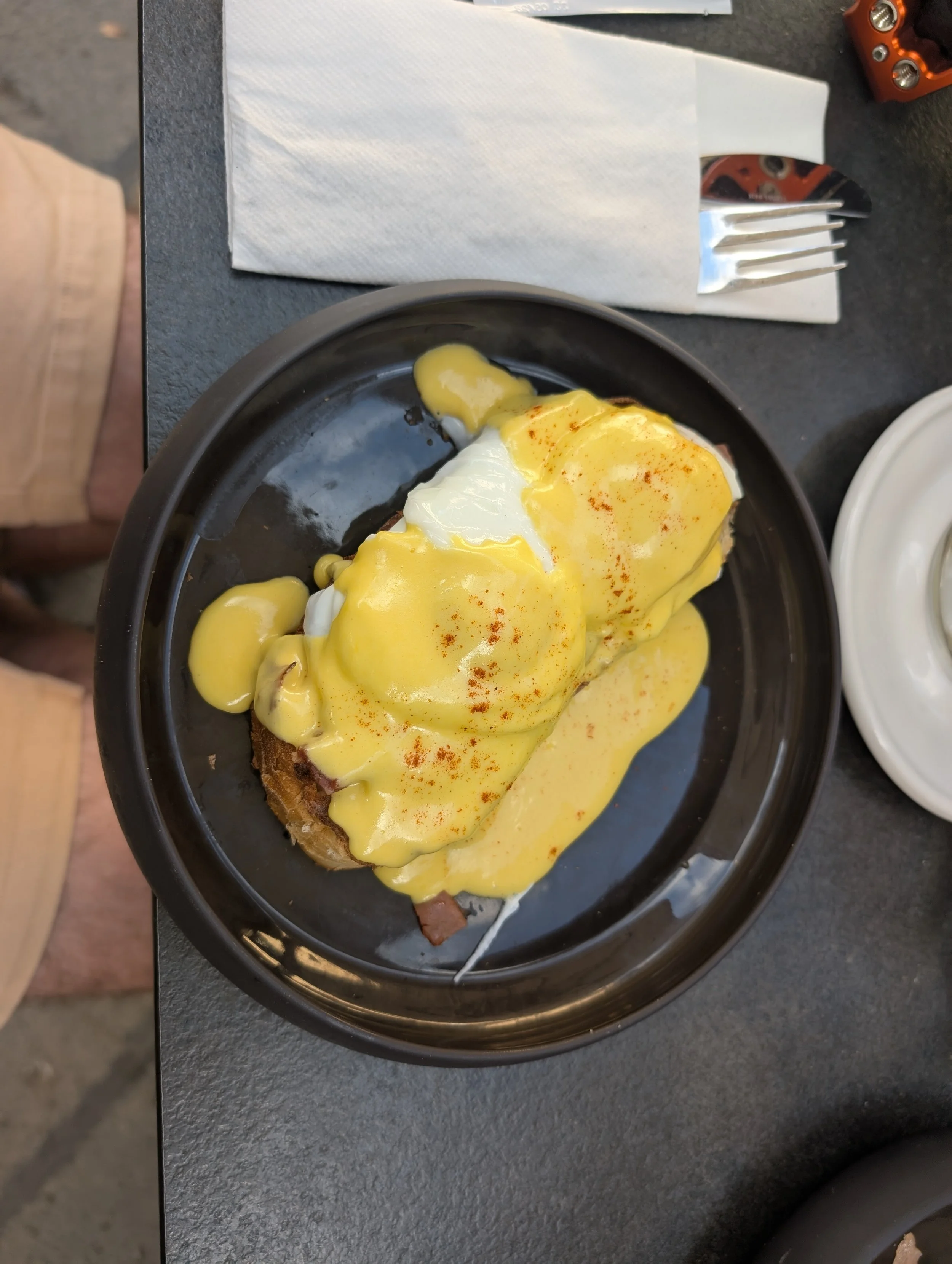 A plate with fried eggs and toast, topped with yellow sauce and sprinkled with paprika, placed on a dark surface.