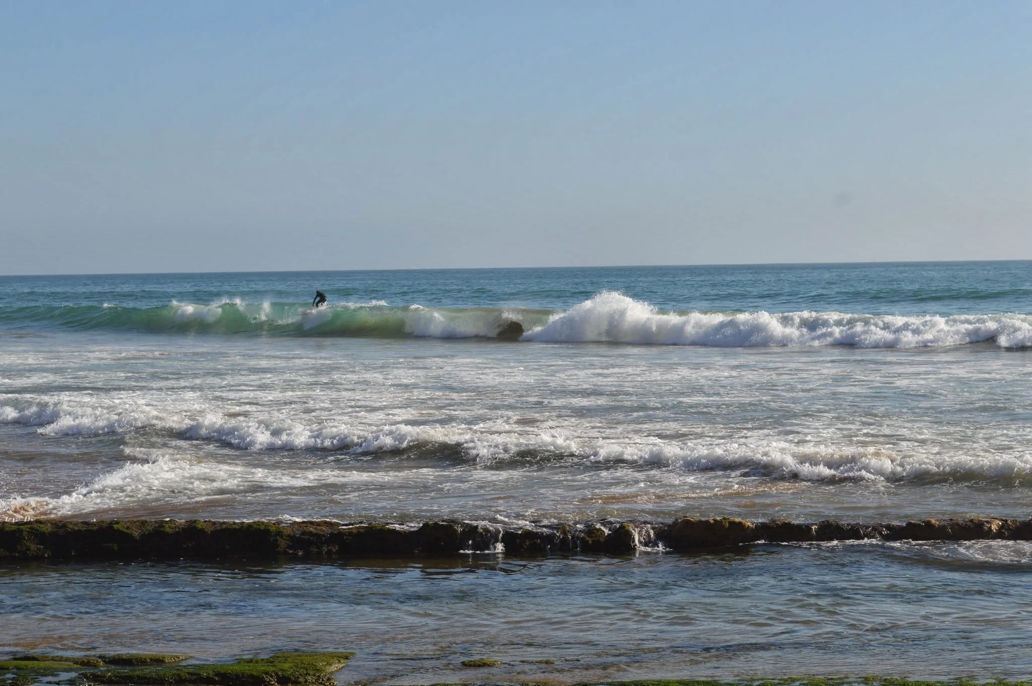 A person surfing on a wave in the ocean near a rocky shoreline.