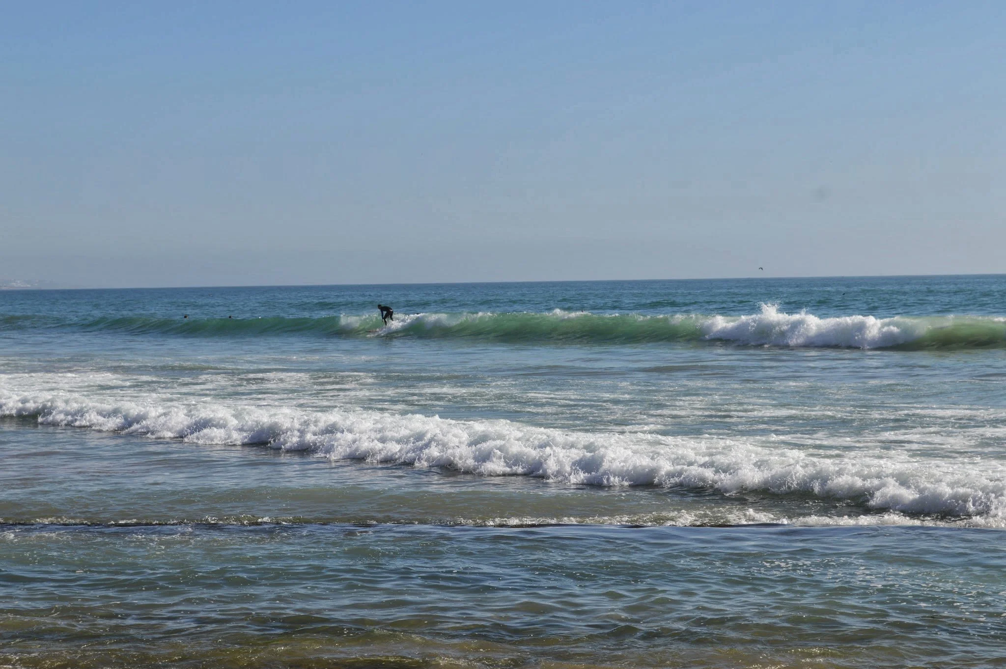 A surfer riding a small wave at the beach on a clear day with blue sky.