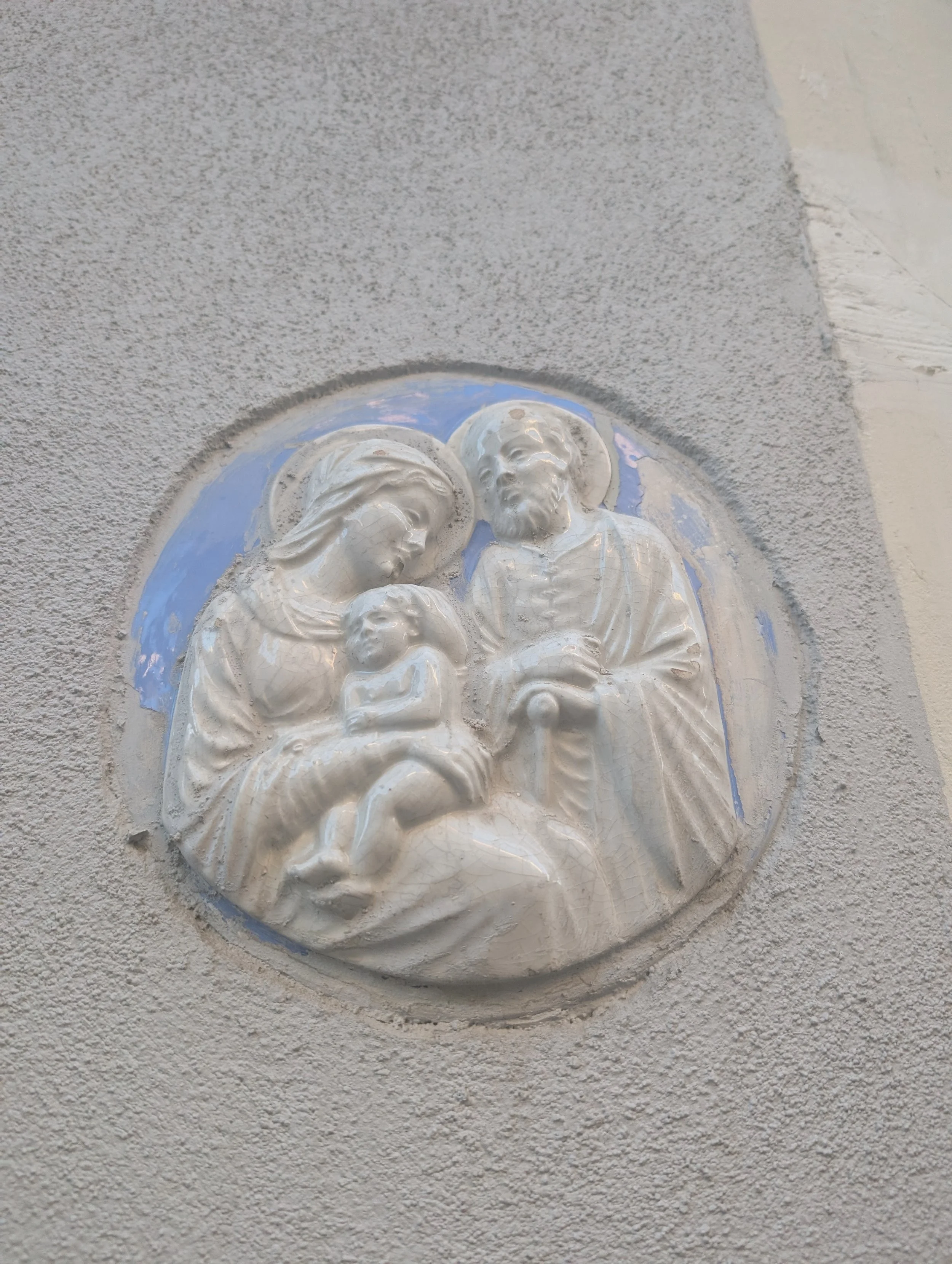 Relief sculpture of Jesus Christ with a halo, holding a child, mounted on a textured wall.