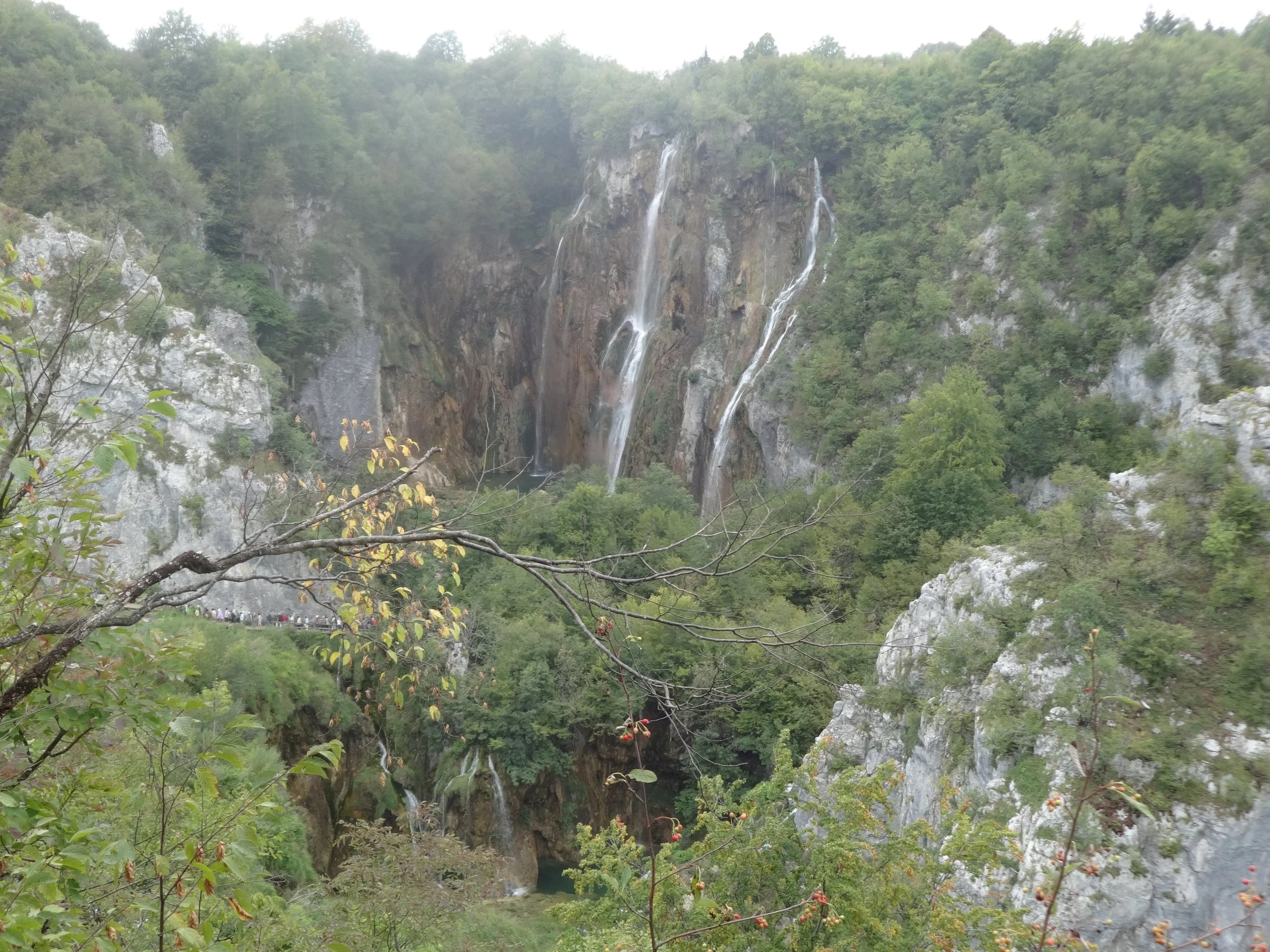 Waterfalls cascading down a rocky cliff surrounded by green trees and foliage.