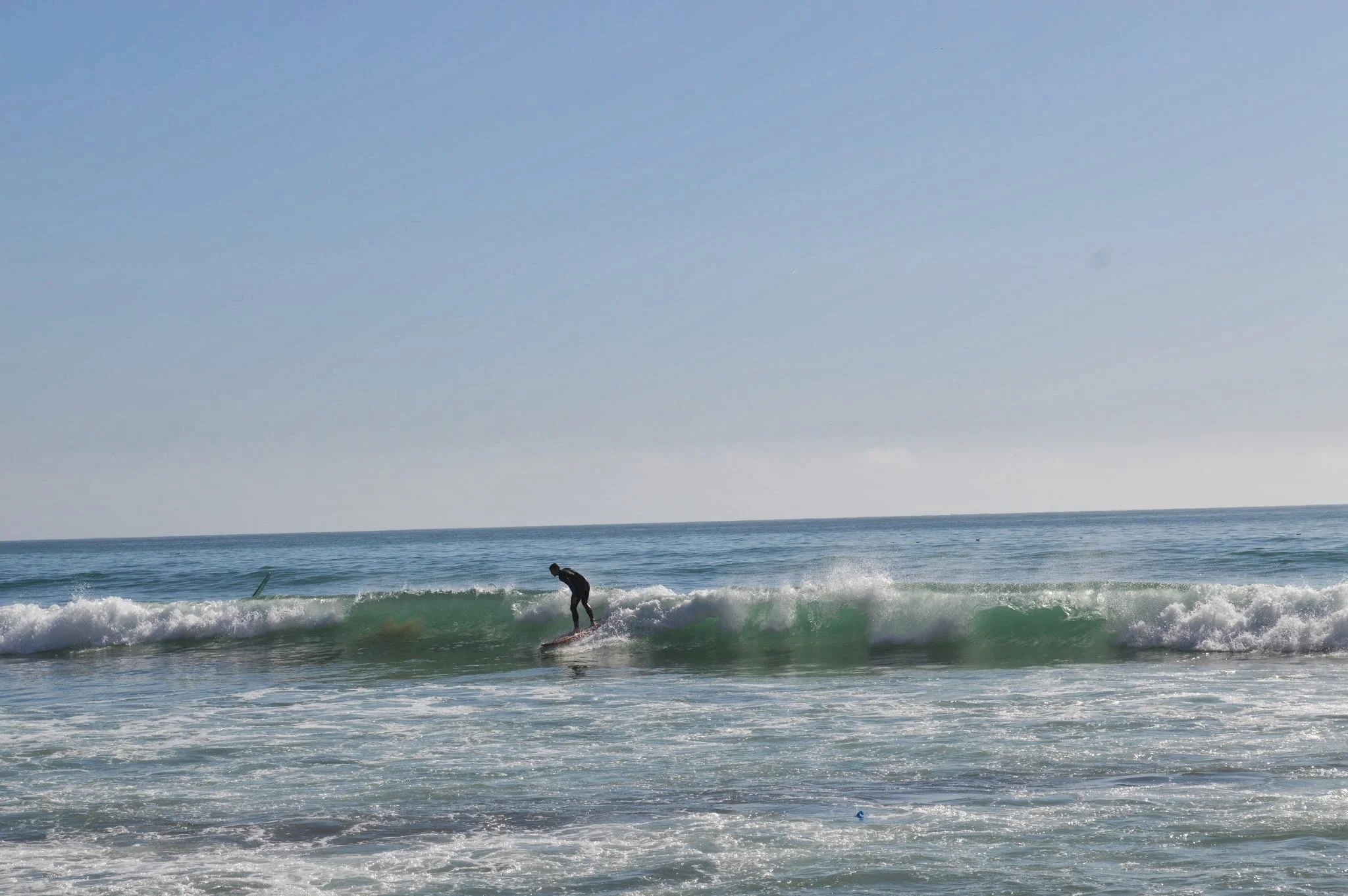 A person surfing on a wave in the ocean with a clear sky above.