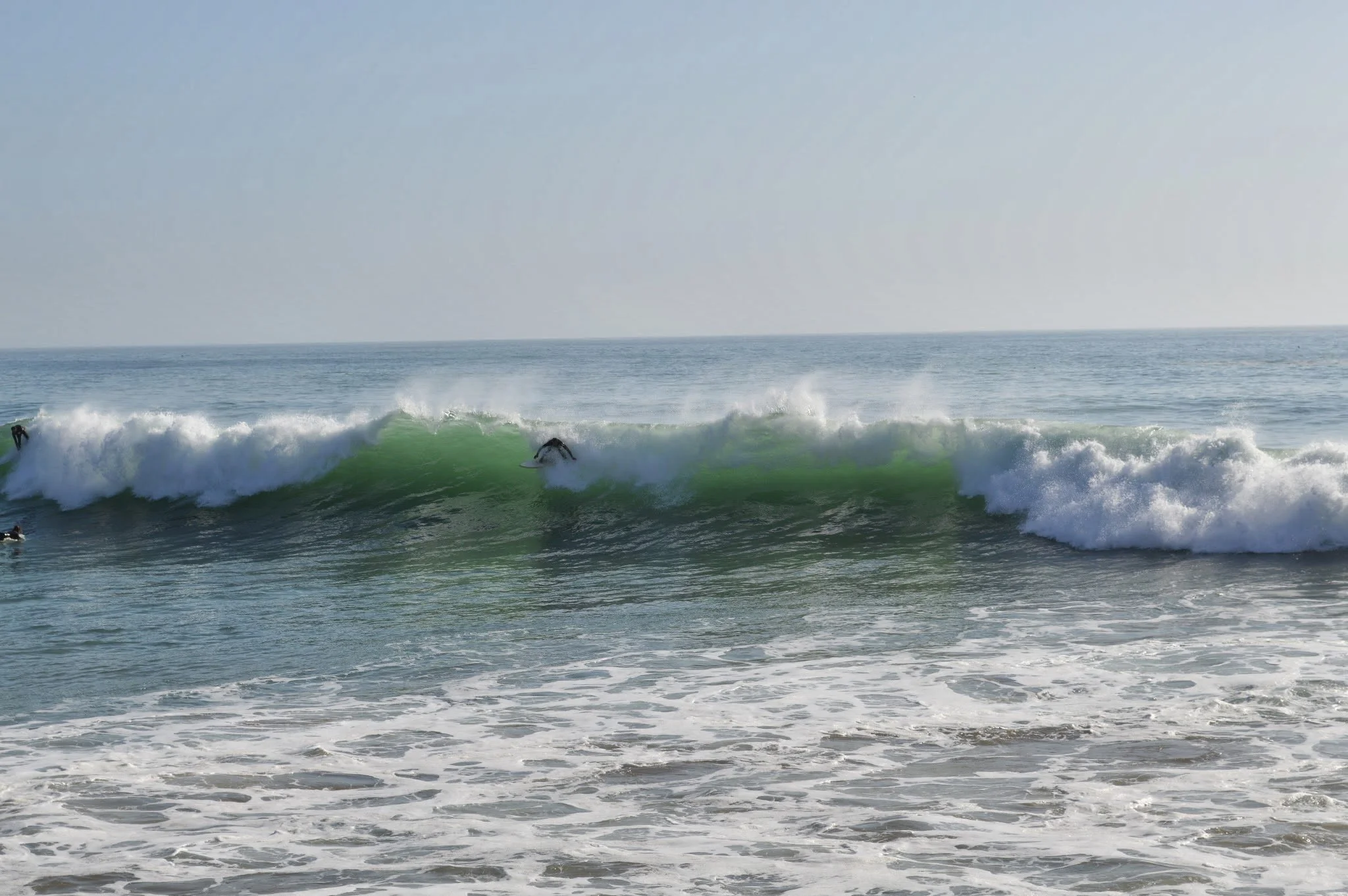 Surfers riding waves close to the shoreline on a clear day in the ocean.