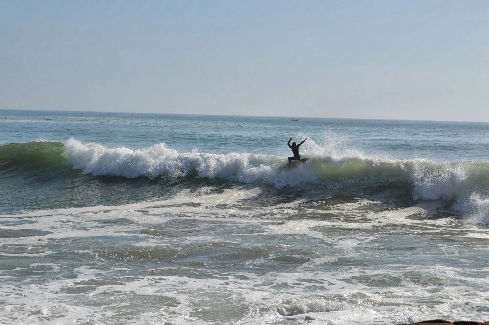 A person surfing on a wave at the beach, with water splashing around them and the ocean extending into the horizon.