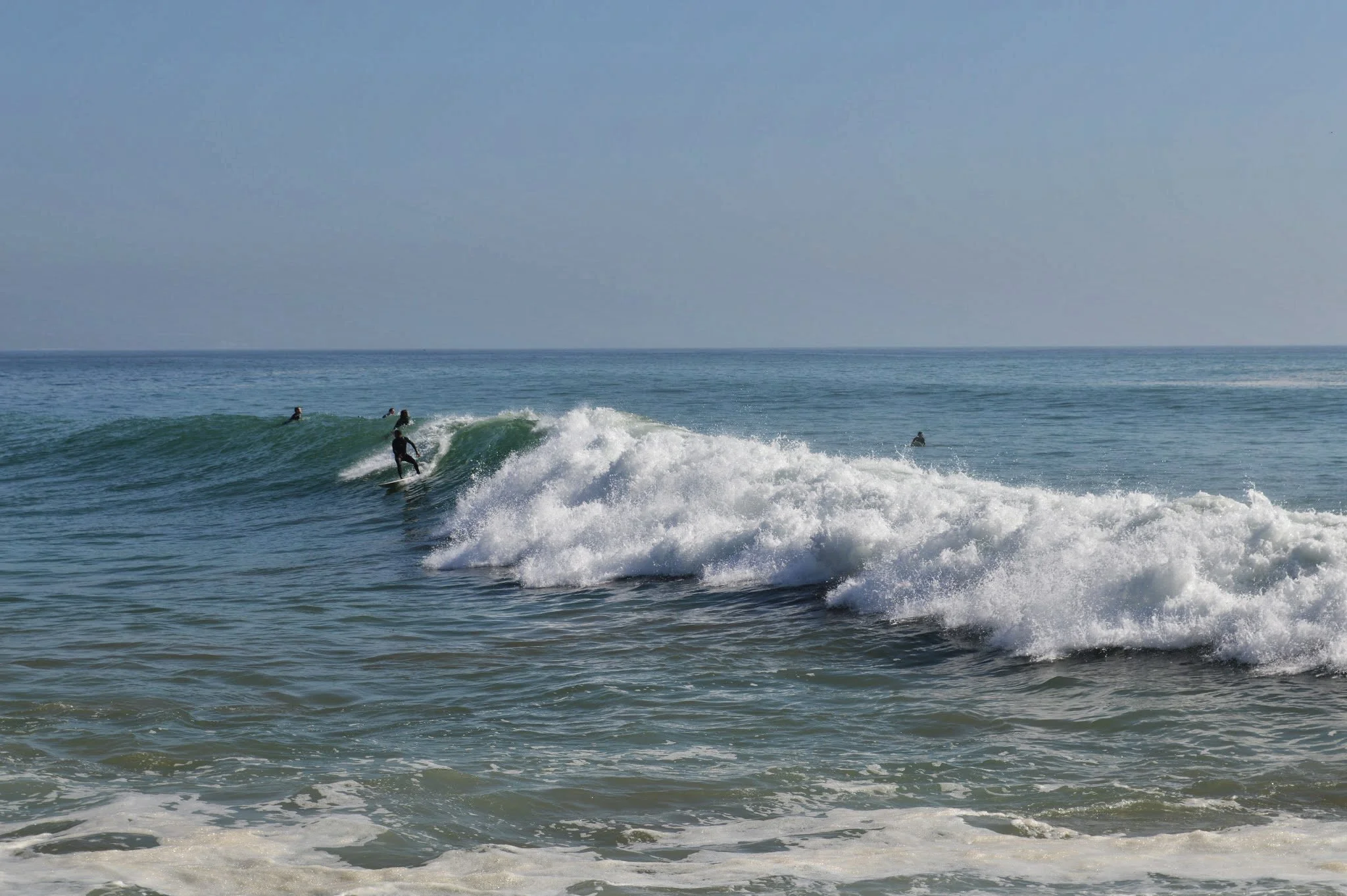 People surfing on ocean waves near the beach on a clear day.