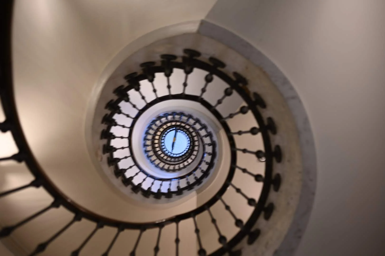 Looking down a spiral staircase with a black metal railing, the photo captures the staircase descending into darkness with a circular shape.