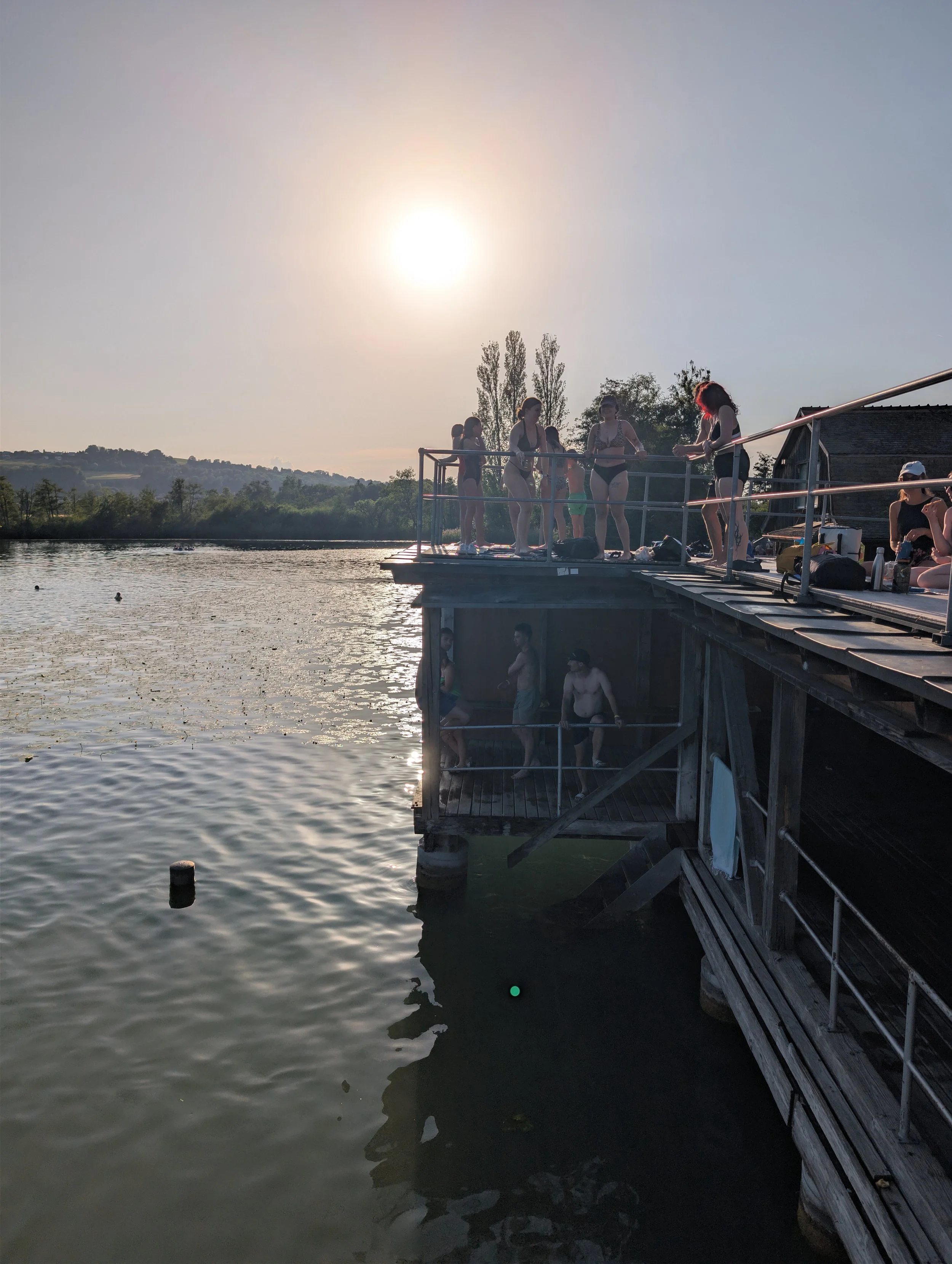 A group of people, mostly women, standing on a boat dock at sunset, preparing to swim in the water.