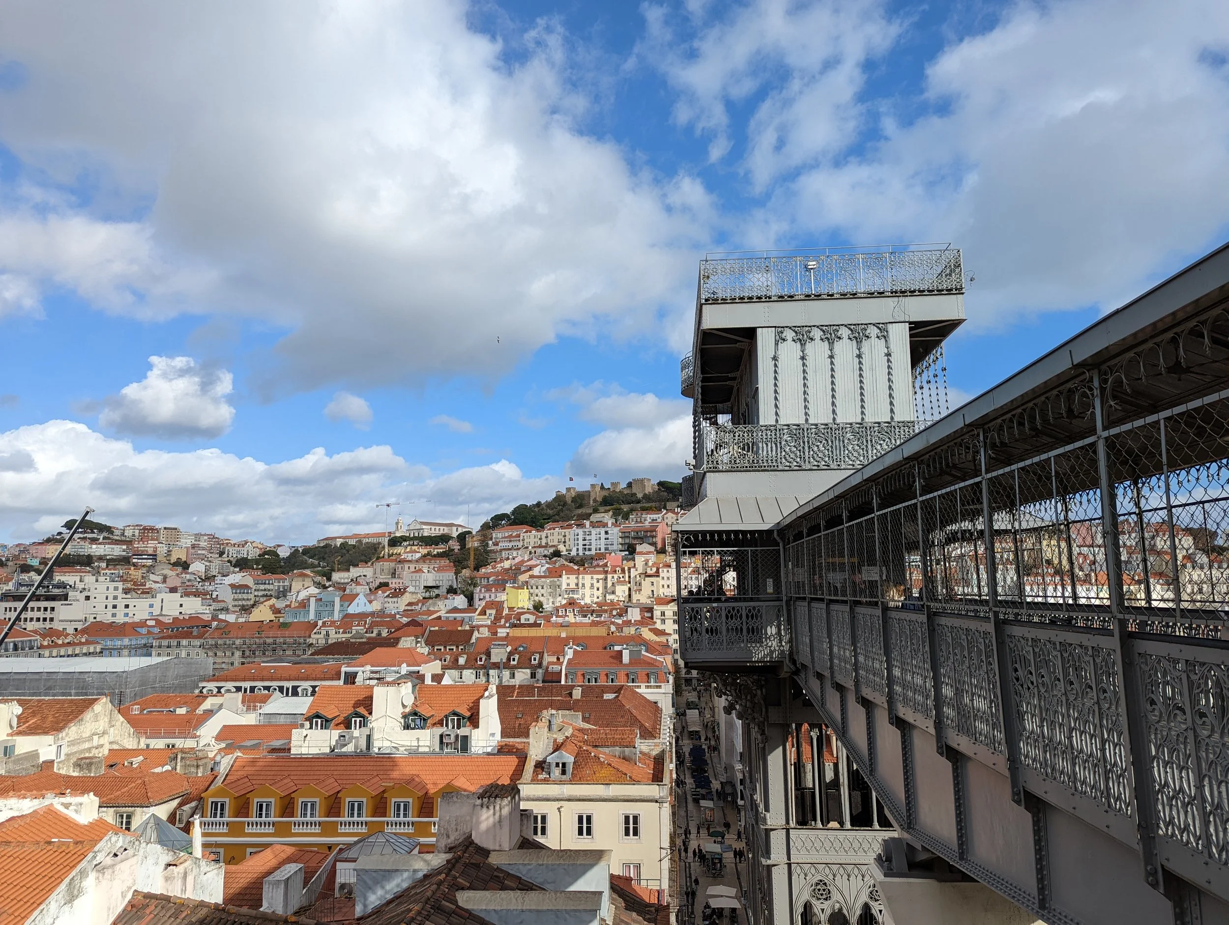 View of rooftops and cityscape under a partly cloudy sky, with a balcony or terrace in the foreground.