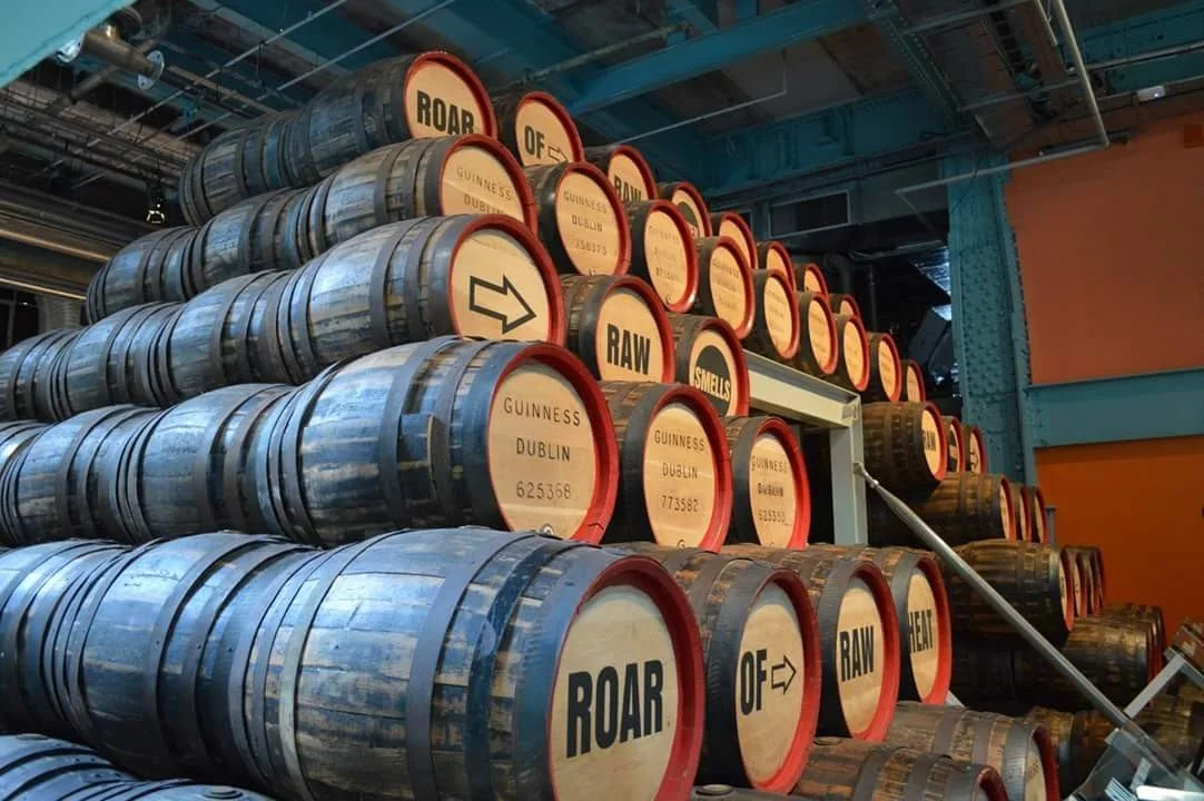Stacked barrels with labels reading 'ROAR OF RAW' and 'GUINNESS DUBLIN' in what appears to be a brewery or warehouse.