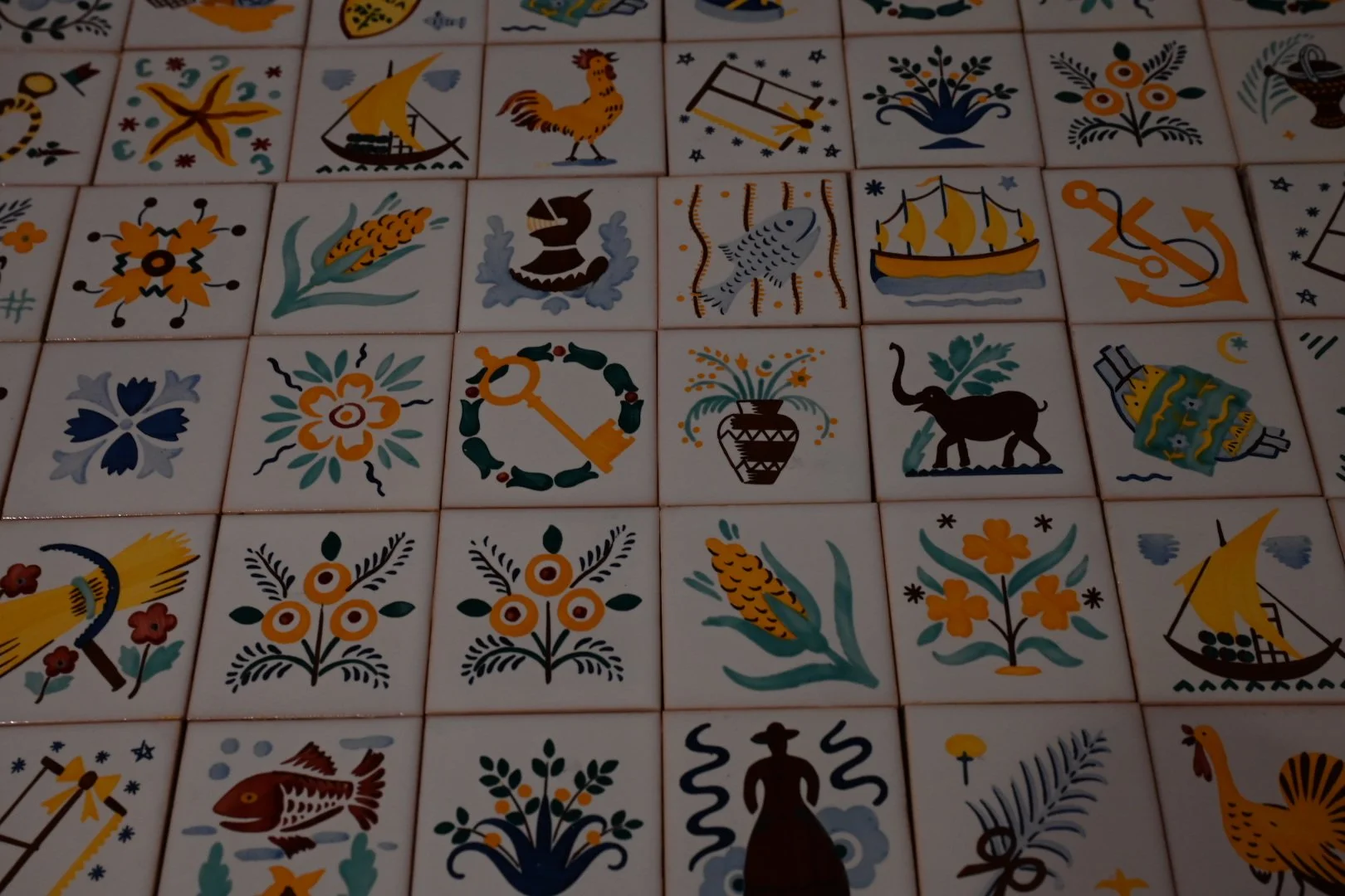 A close-up view of decorated tiles with traditional folk art designs featuring flowers, animals, and boats, arranged in a grid pattern.