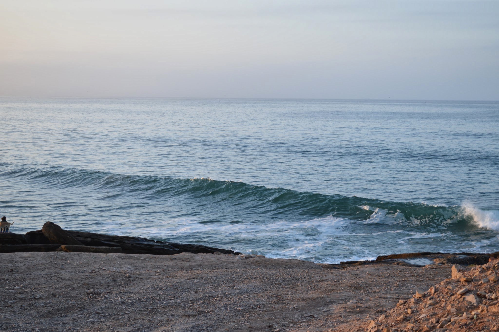 Ocean waves crashing onto a rocky shoreline under a cloudy sky.