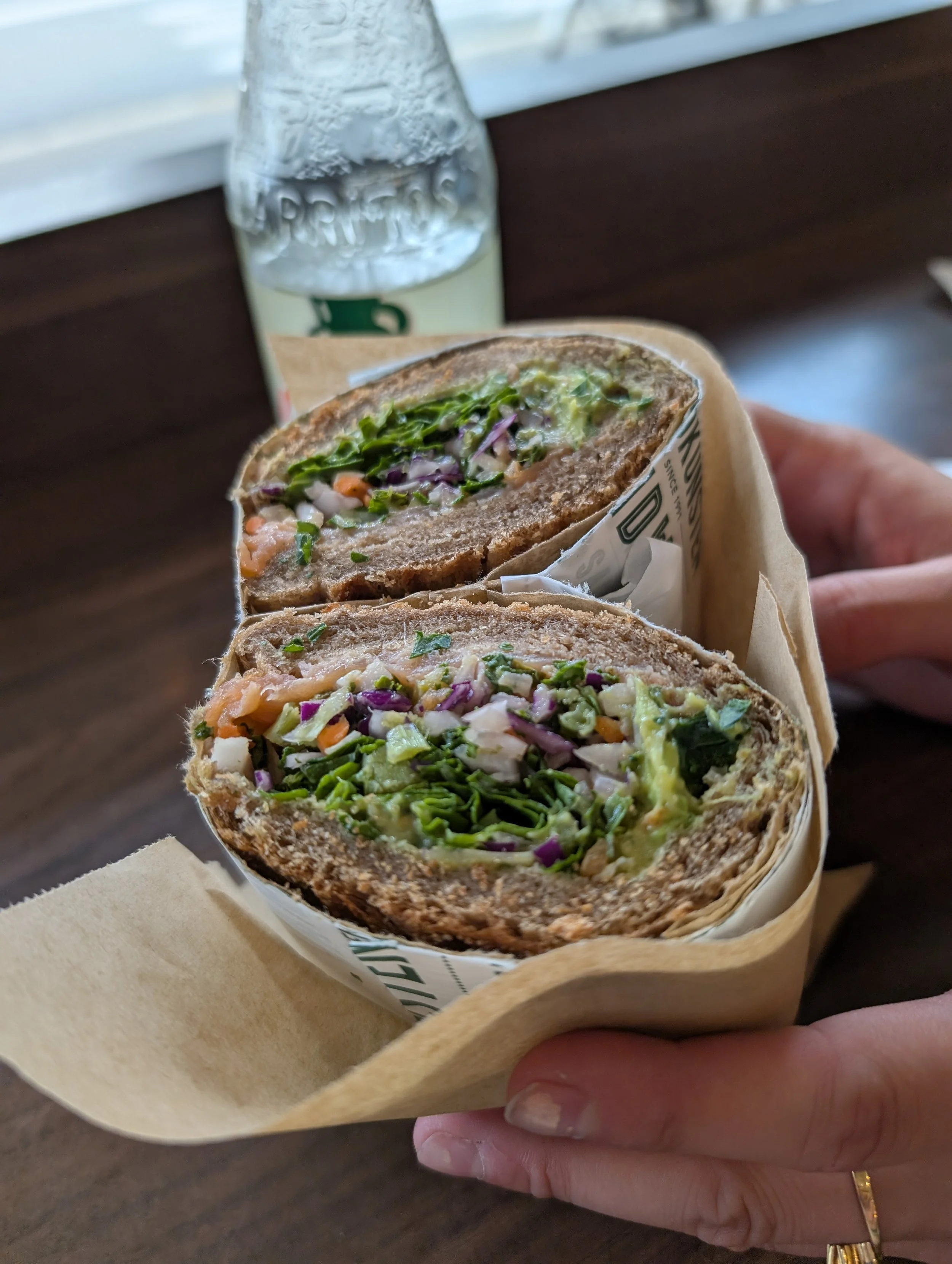Close-up of a hand holding a cut vegetable wrap sandwich, with a bottle of water in the background.