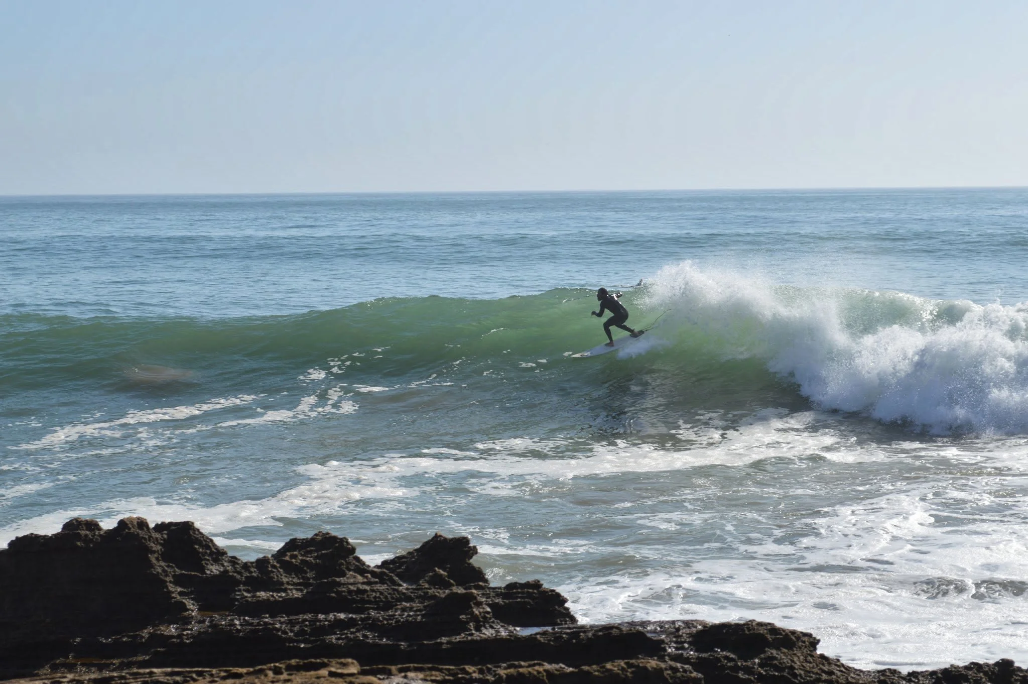 A person surfing on a wave near a rocky shoreline in the ocean.