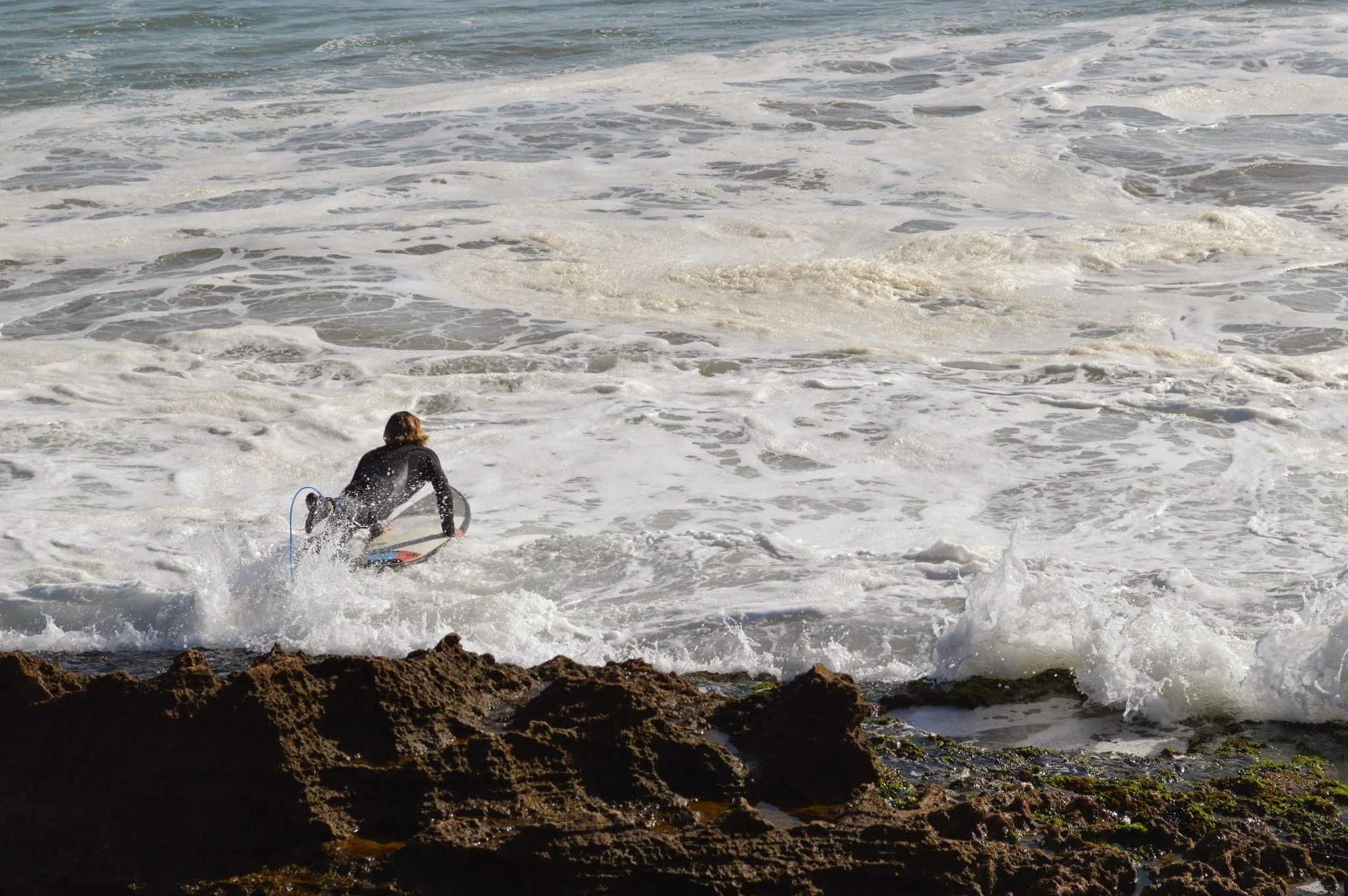 A person in a wetsuit riding a surfboard on the ocean waves near a rocky shoreline.