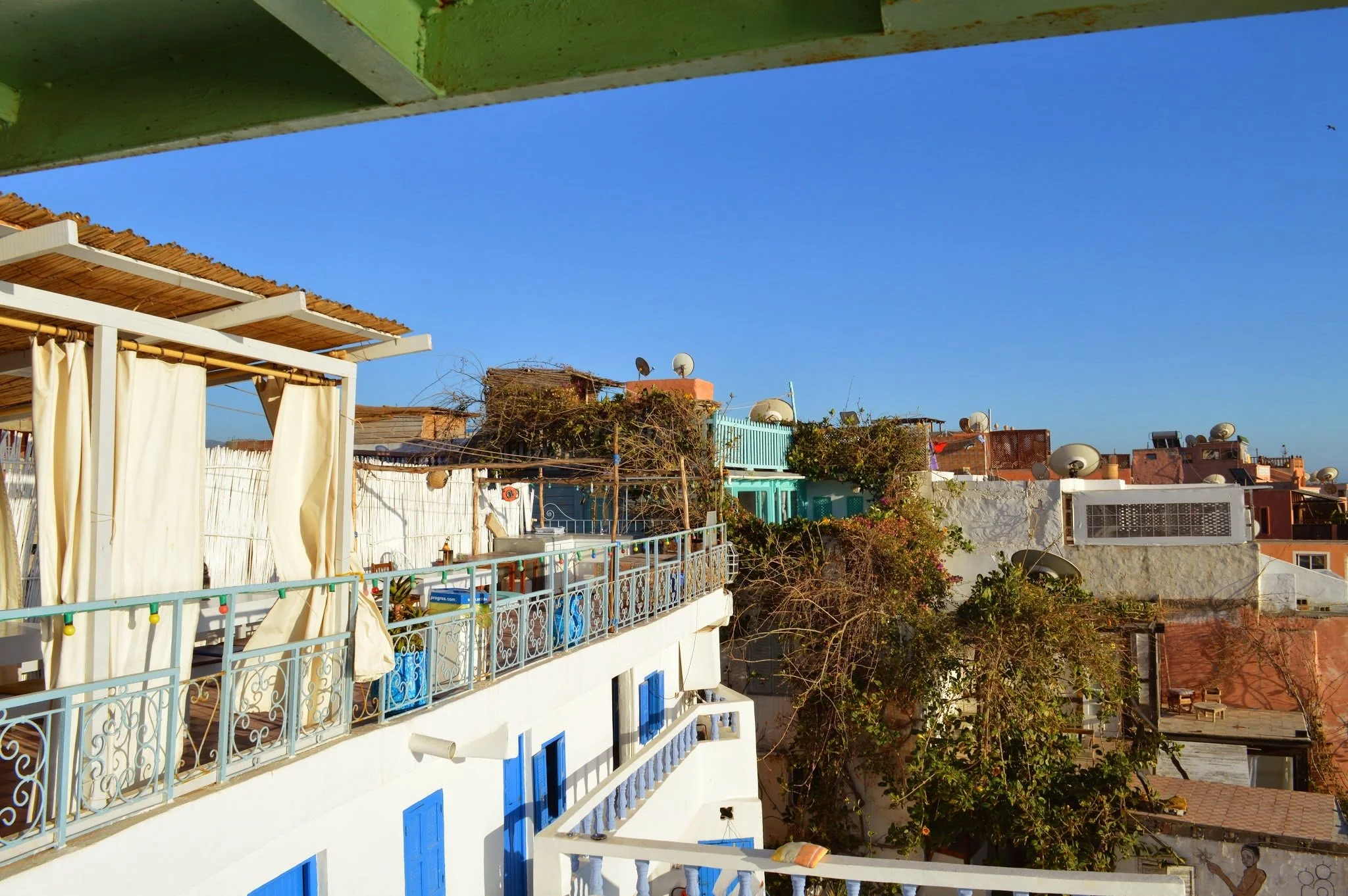 A view of rooftop buildings with satellite dishes, trees, and a clear blue sky.