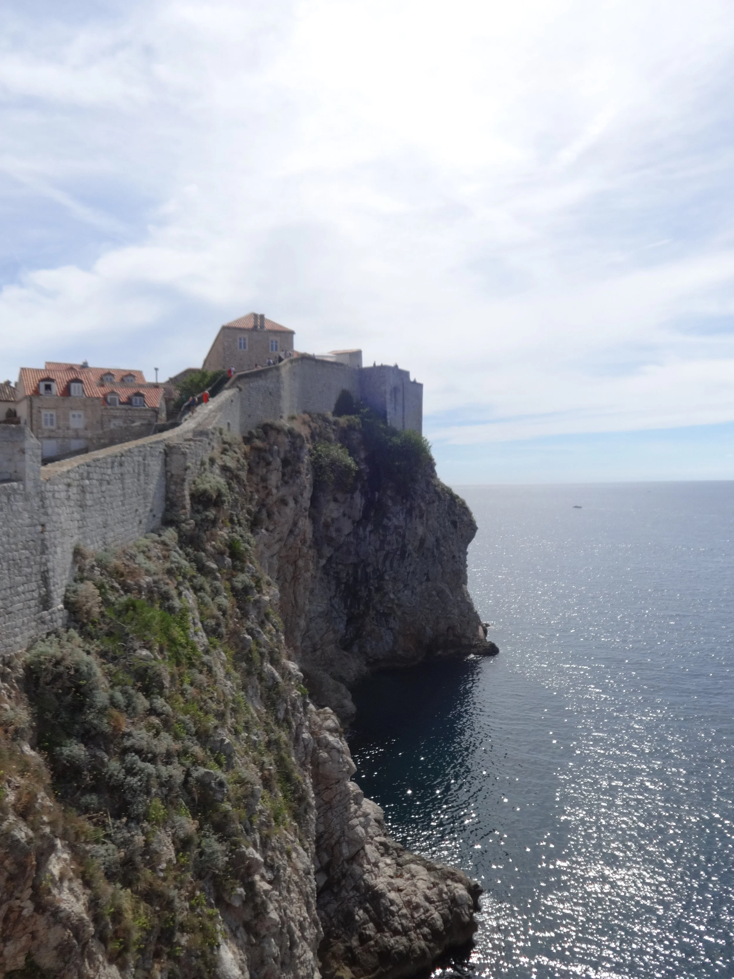 Cliffside with historic stone buildings overlooking the ocean, under a partly cloudy sky.