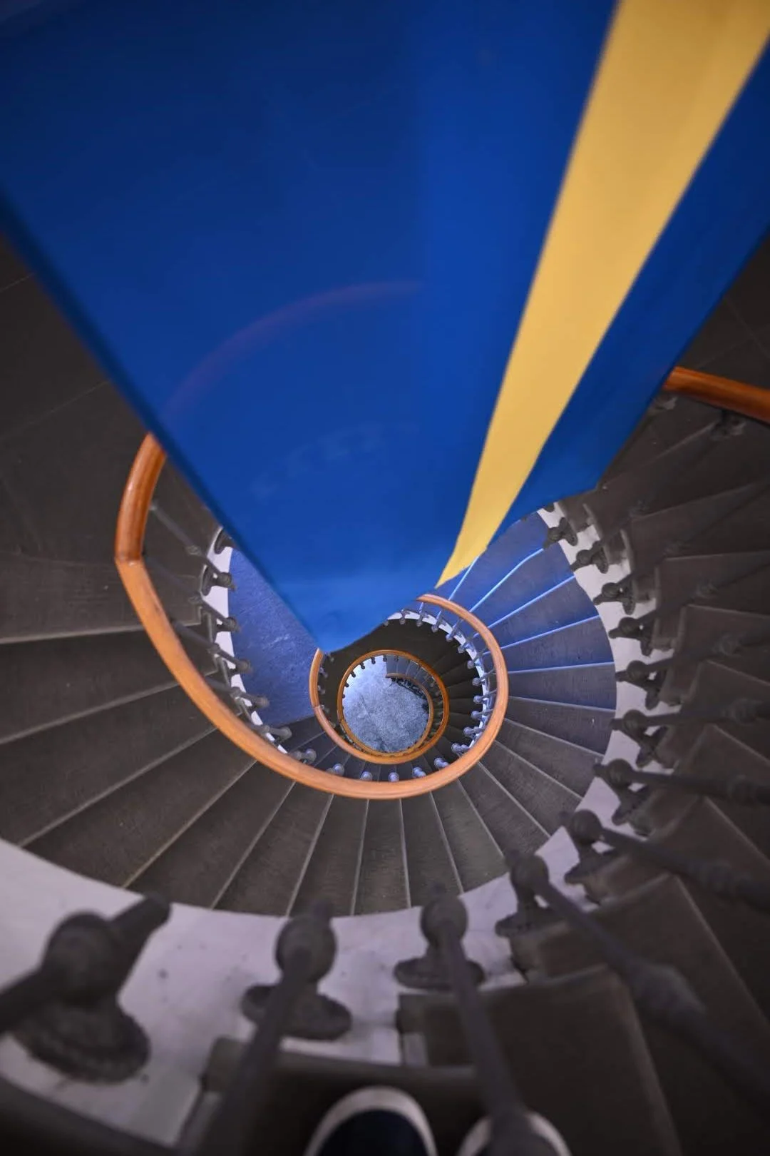 View looking down a spiral staircase with black steps, a blue and yellow banister, and black railings.