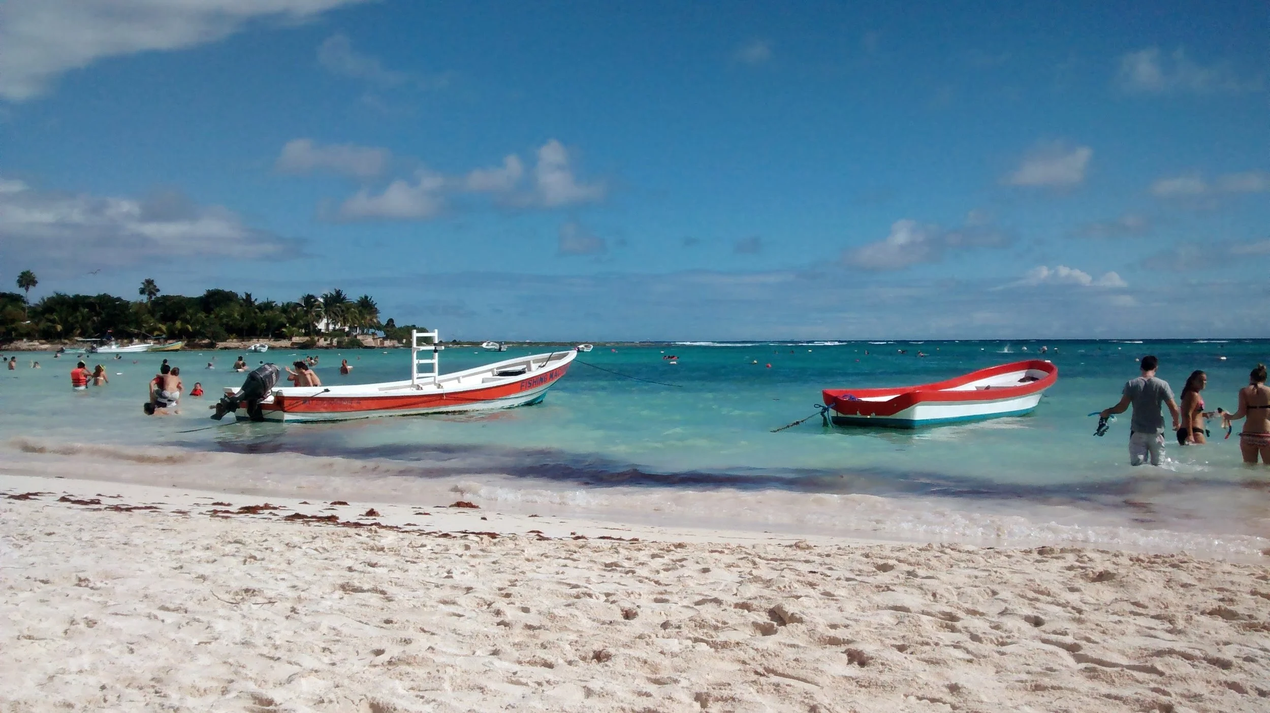 Beach with people swimming and relaxing, boat with outboard motor, and clear blue sky.