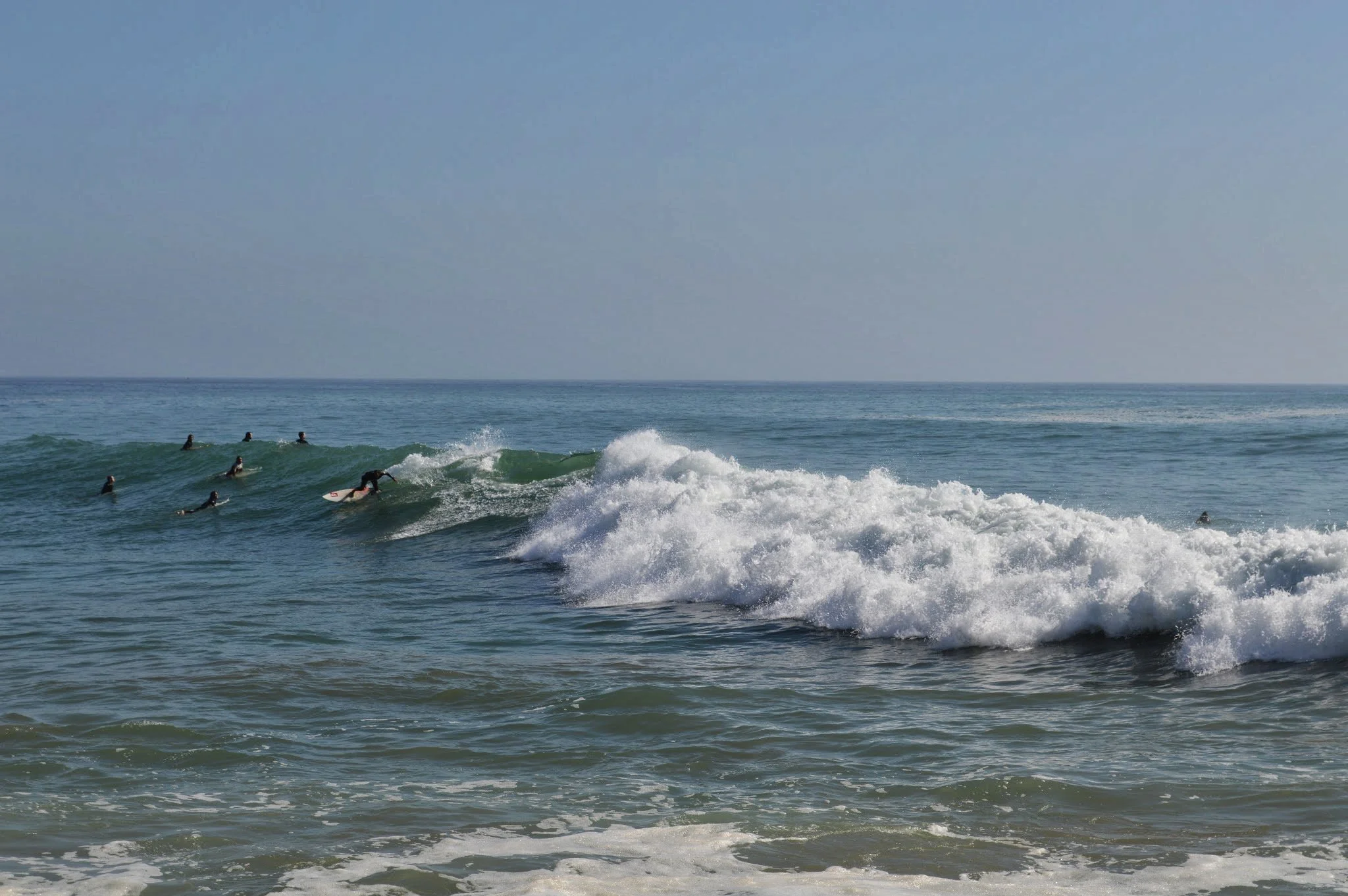 Several surfers in wetsuits riding waves in the ocean under a clear sky.