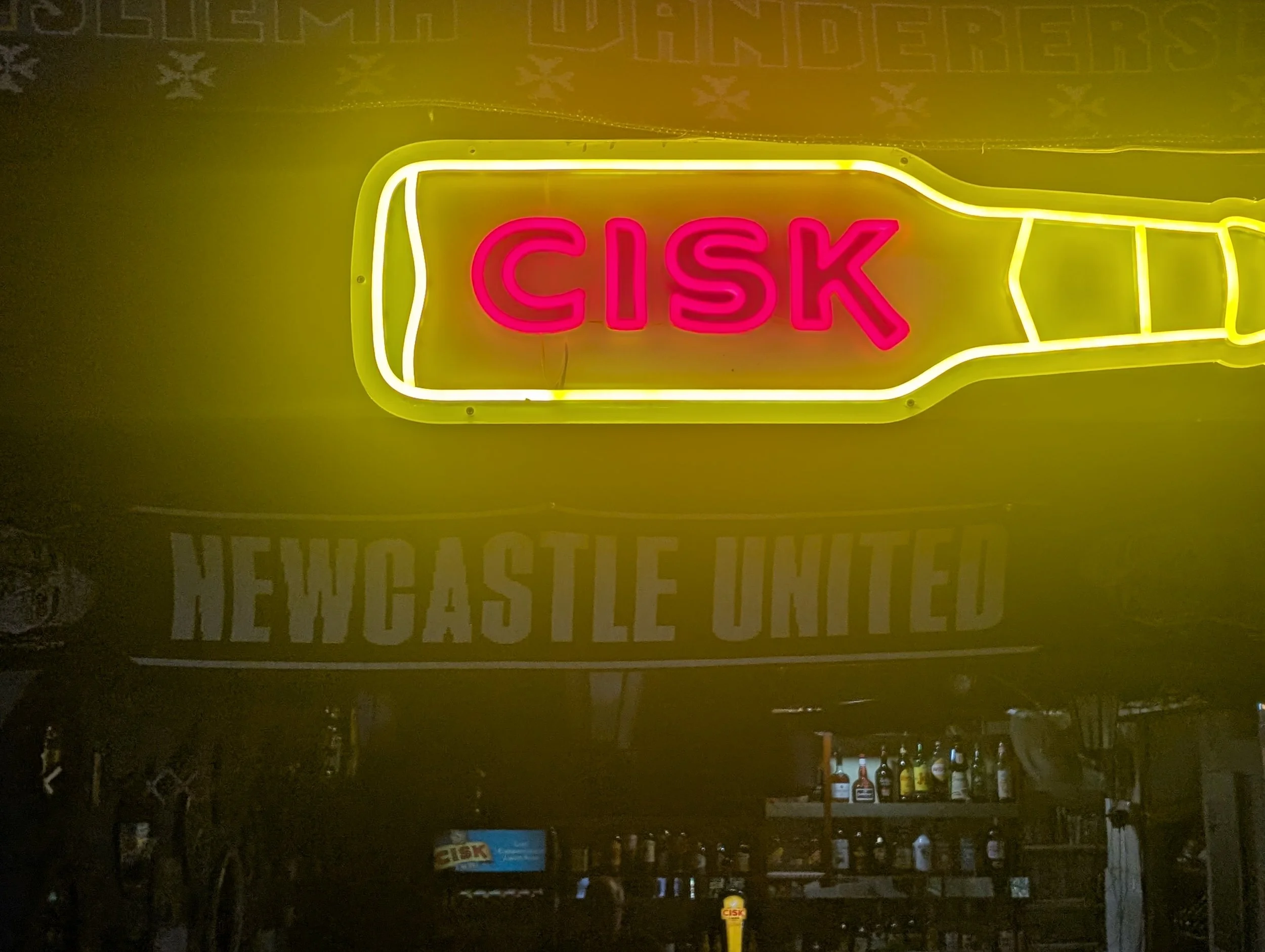 A neon sign with the word 'CISK' in bright pink letters outlined in yellow, mounted on a dark background, likely in a bar or pub setting.