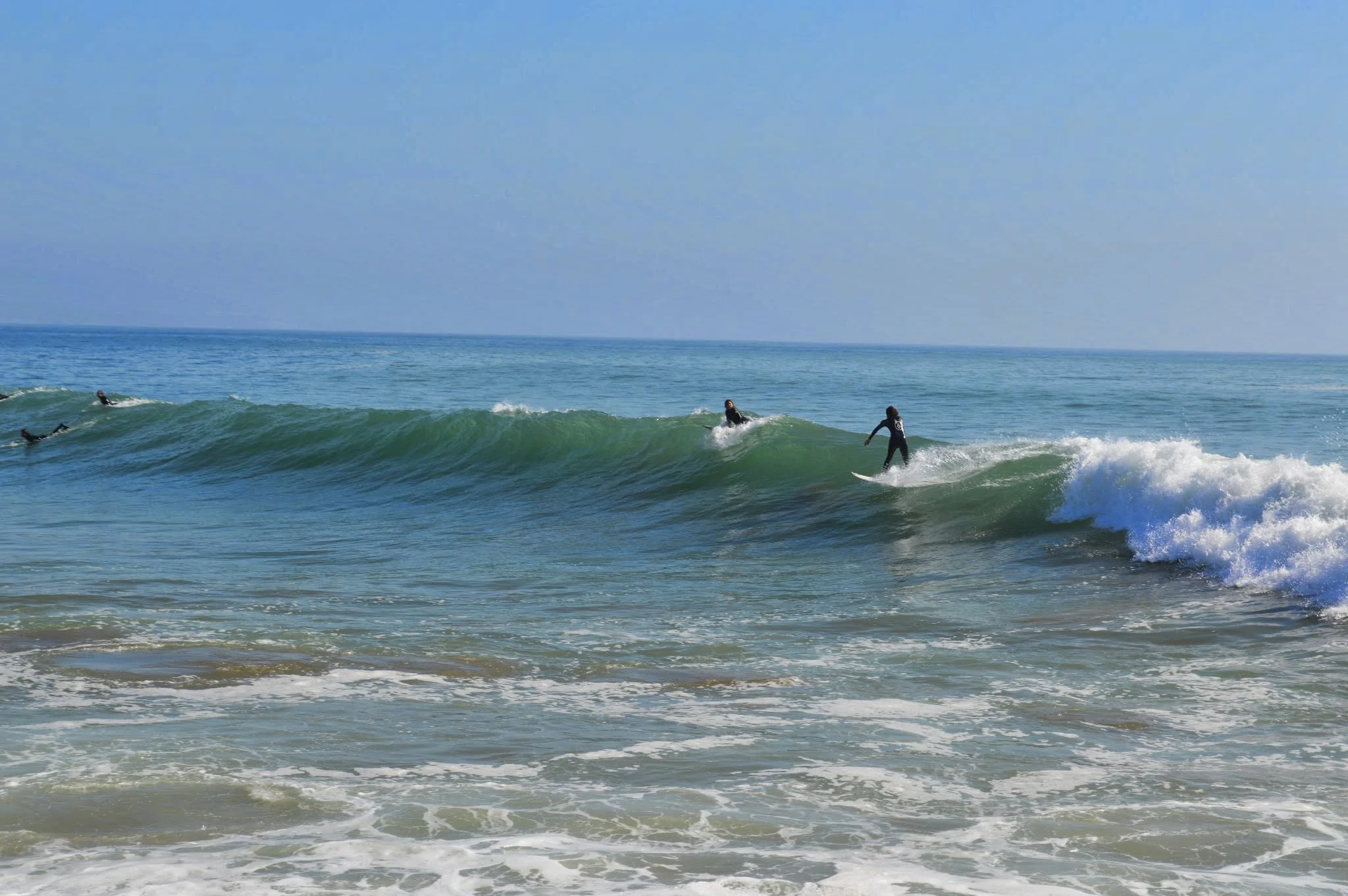 People surfing on ocean waves near the shore with a clear blue sky overhead.