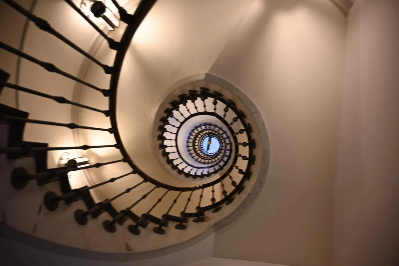 A spiral staircase viewed from above, with a clock visible at the center of the spiral.