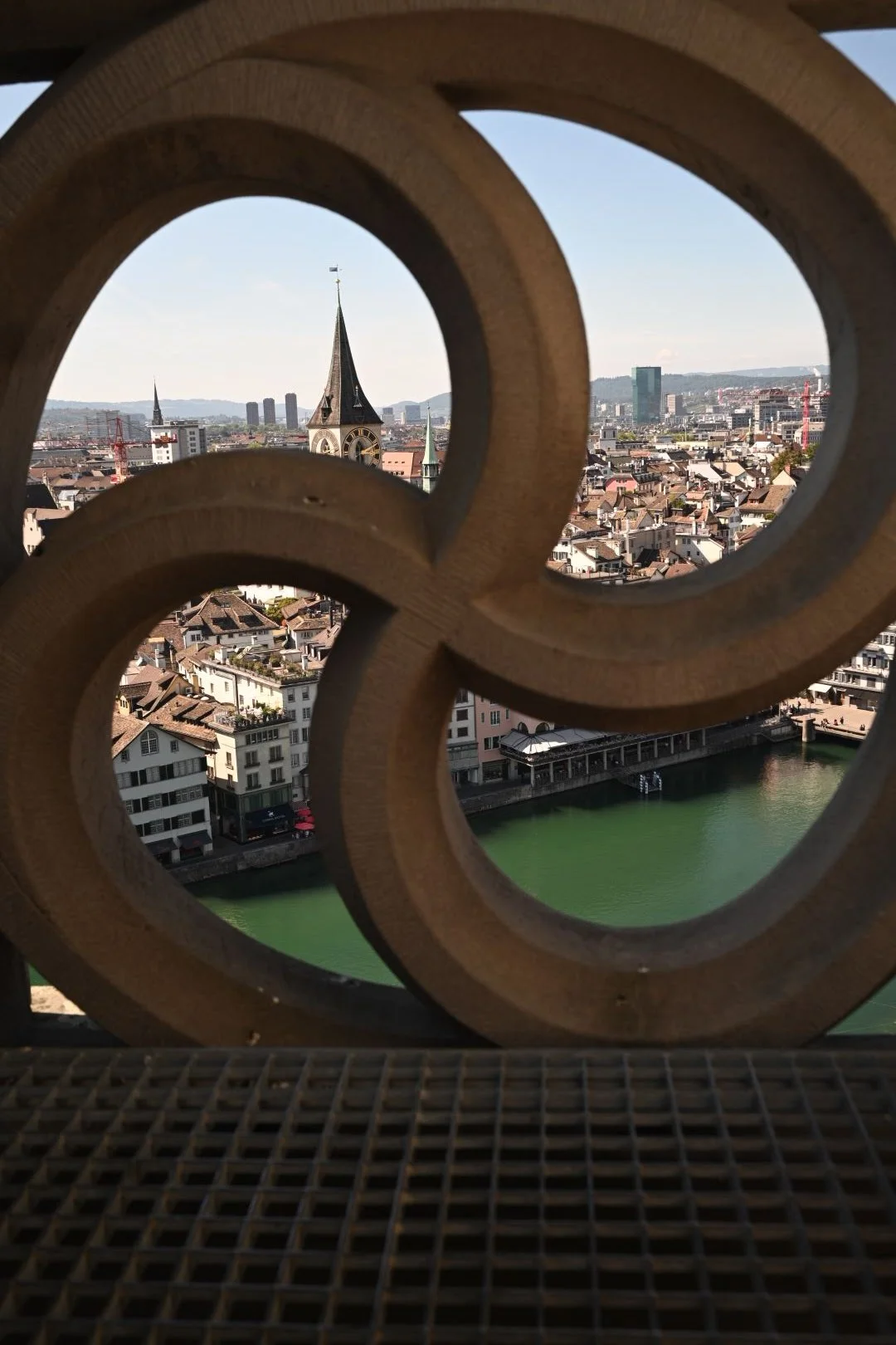 View of a city with a river, a church steeple, and modern buildings seen through a decorative wooden lattice.