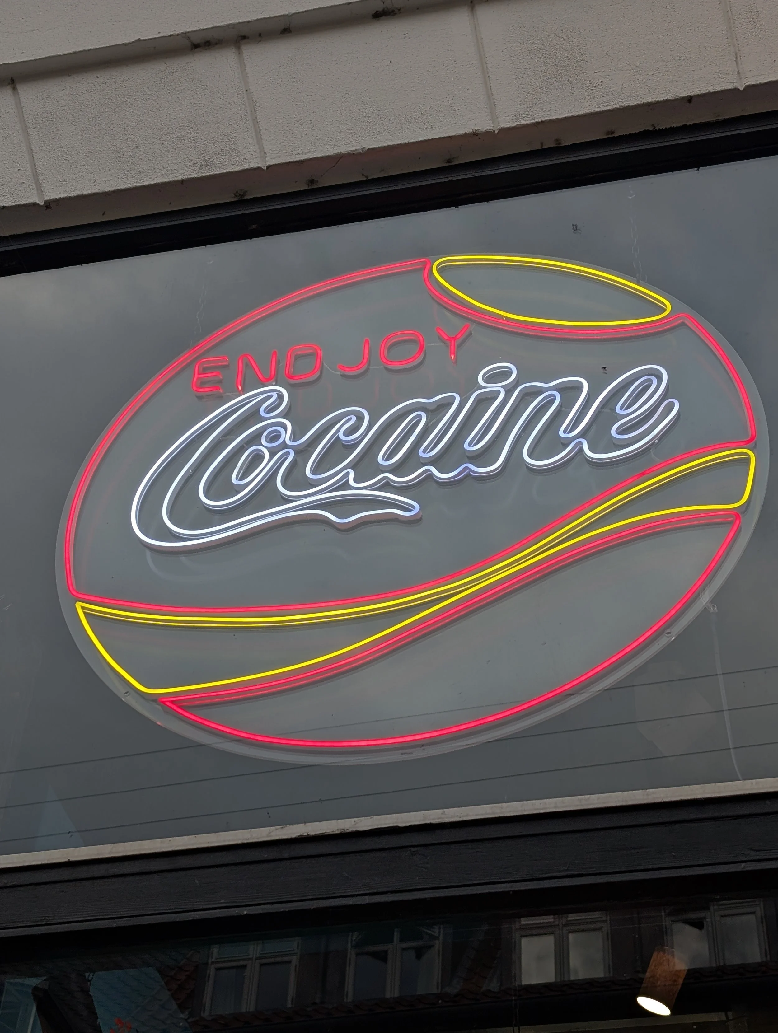 Neon sign with the word 'Enjoy' in red and 'Coca-Cola' in white, surrounded by a yellow and red outline resembling a bottle cap.