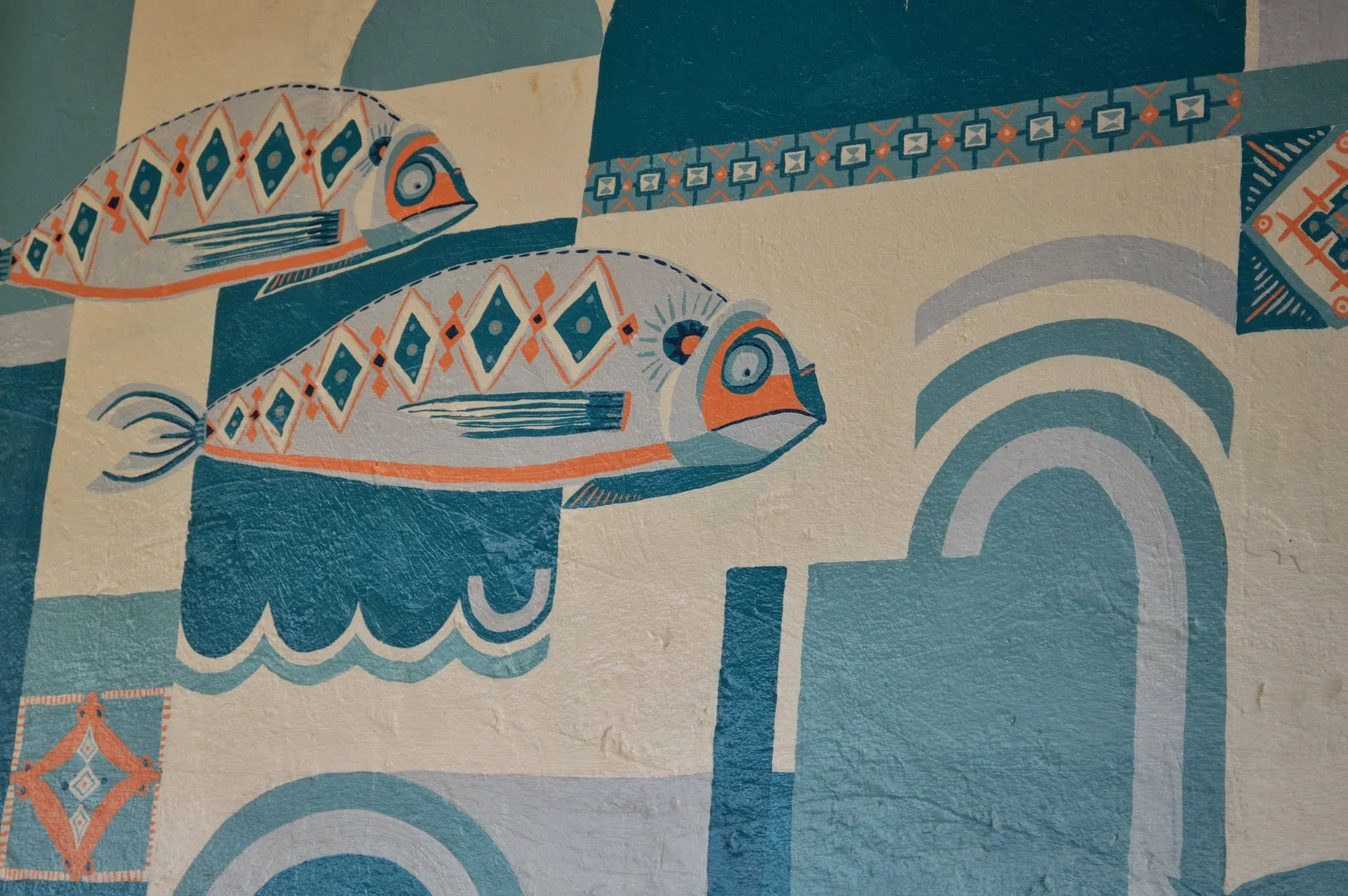 A mural featuring two stylised fish with geometric patterns and orange, blue, and white colours, along with some decorative elements and patterns in the background.