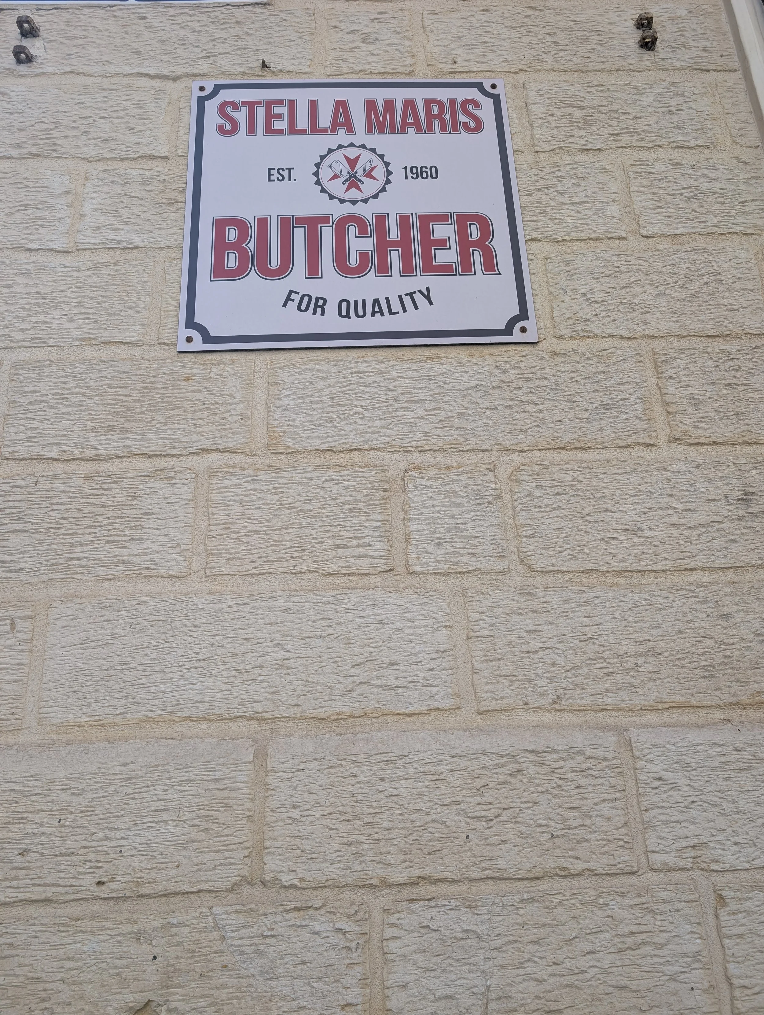 Sign on a brick wall for 'Stella Maris Butcher,' established in 1960, emphasizing quality.