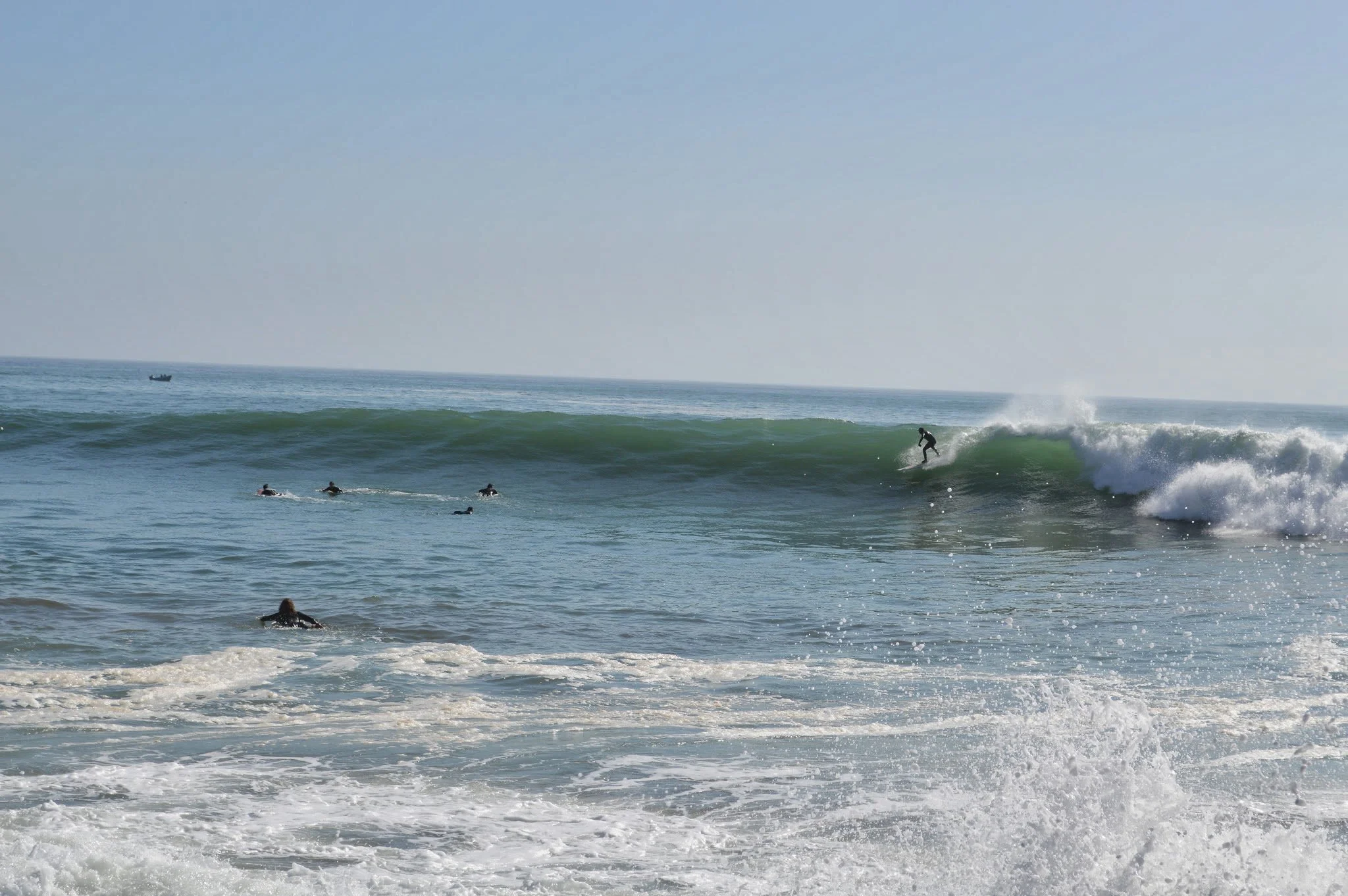 Surfers in wetsuits riding and waiting for waves at the beach as the ocean waves crash.