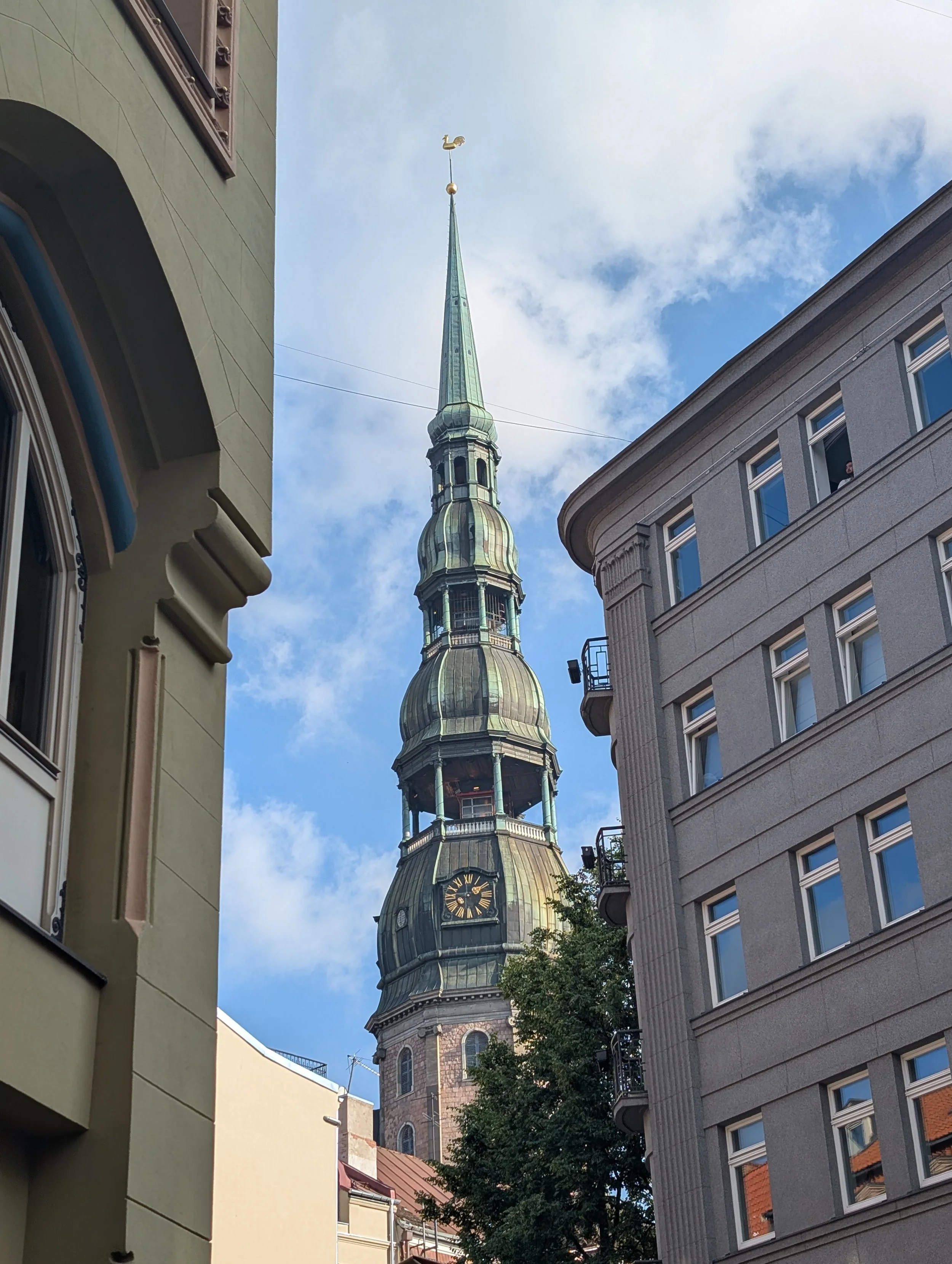View of a historic church tower with a clock, framed by modern buildings on either side.
