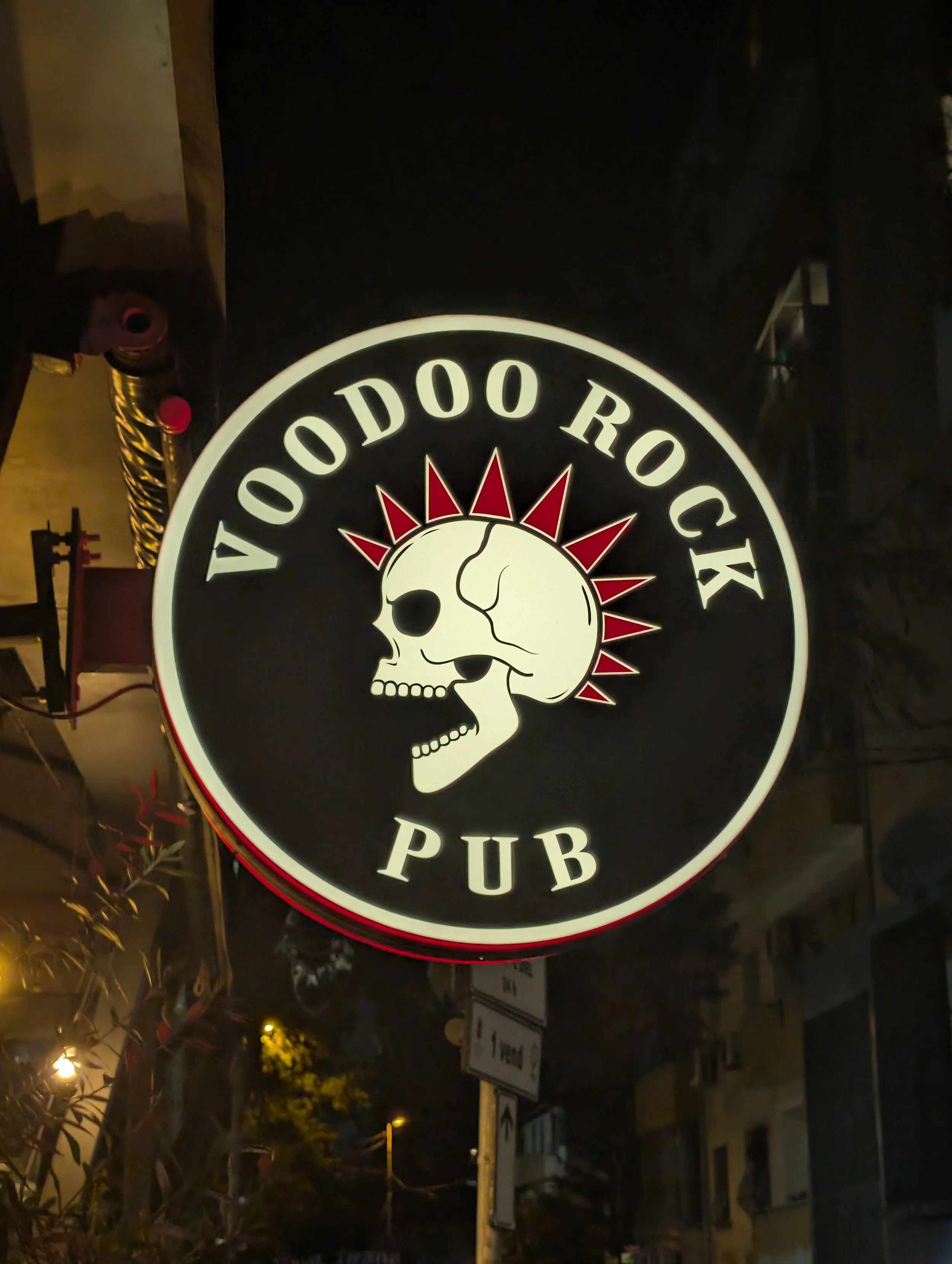 Sign for Toyoodoo Rock Pub featuring a skull with a sunburst design in the background, illuminated at night.