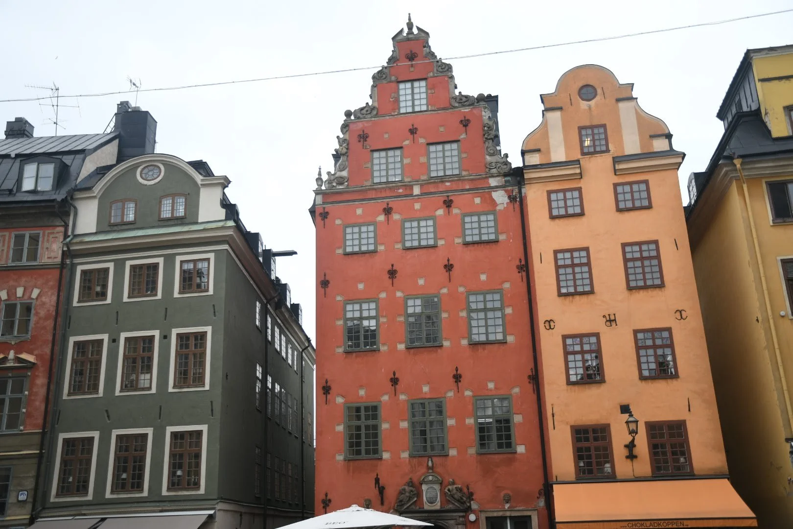 Colorful historic buildings in a European city, featuring ornate architecture and window designs, with a cloudy sky overhead.