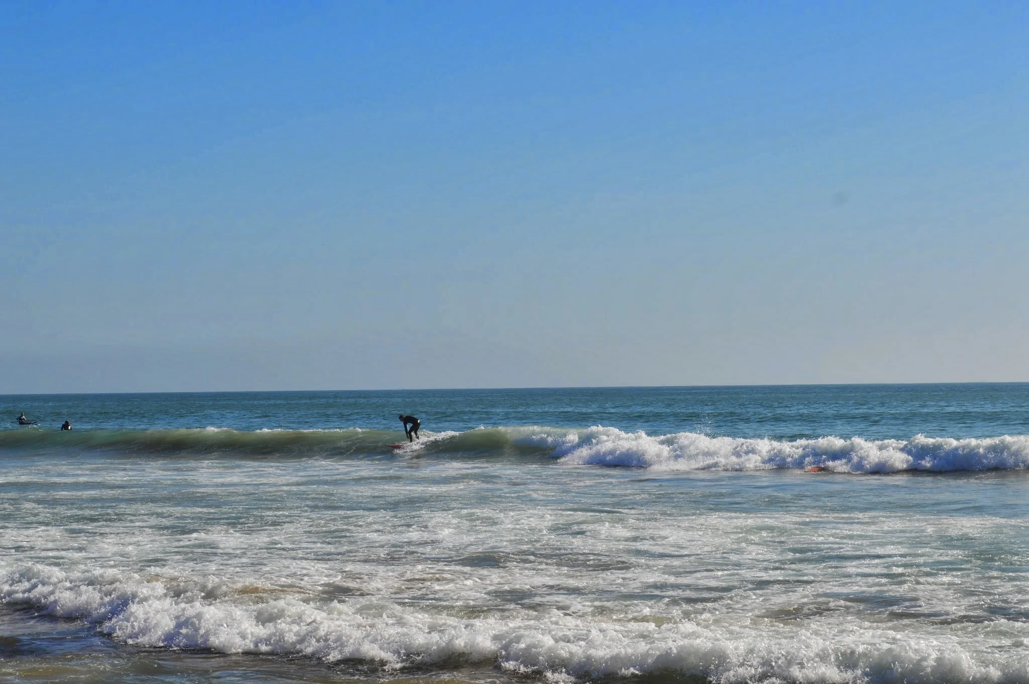 People surfing on the ocean waves near the shore with a clear blue sky overhead.