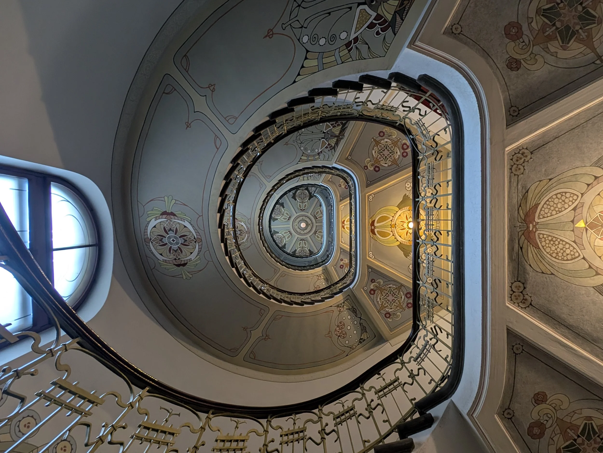 A spiral staircase with decorative painted walls and ornate railings, viewed from below.