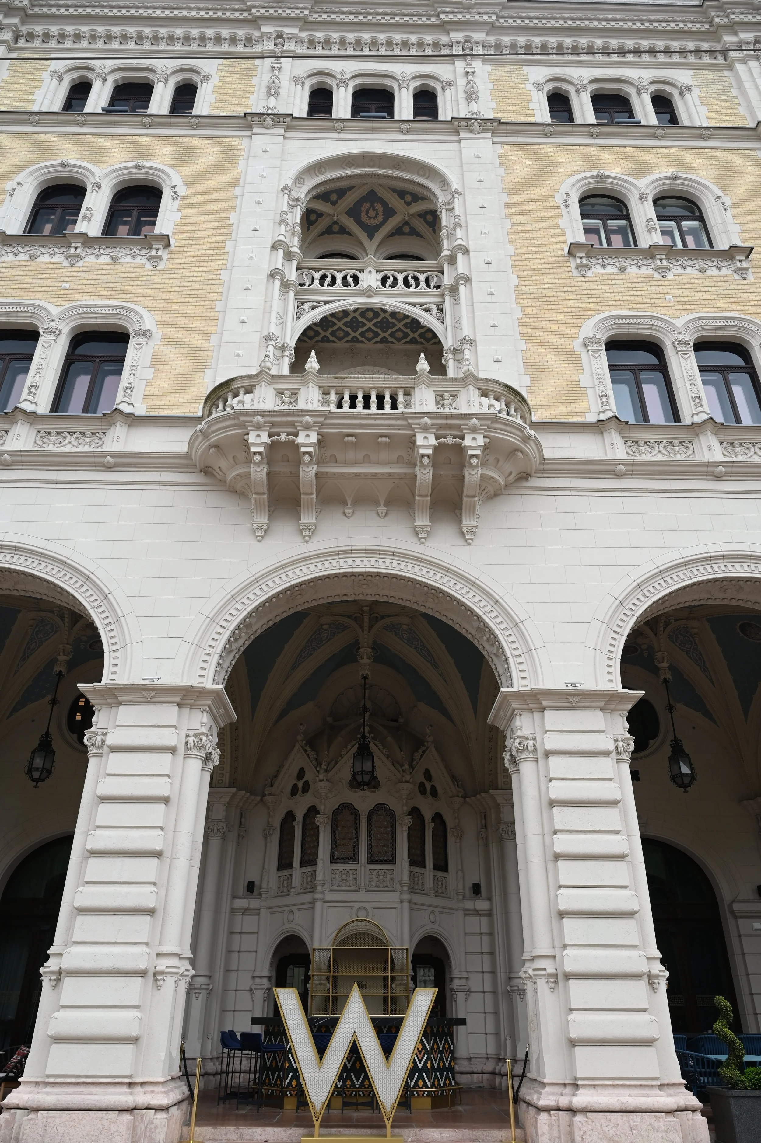 A historic building with ornate architectural details, including arched windows, decorative columns, and a balcony. There is a large illuminated letter 'W' in front of the entrance.