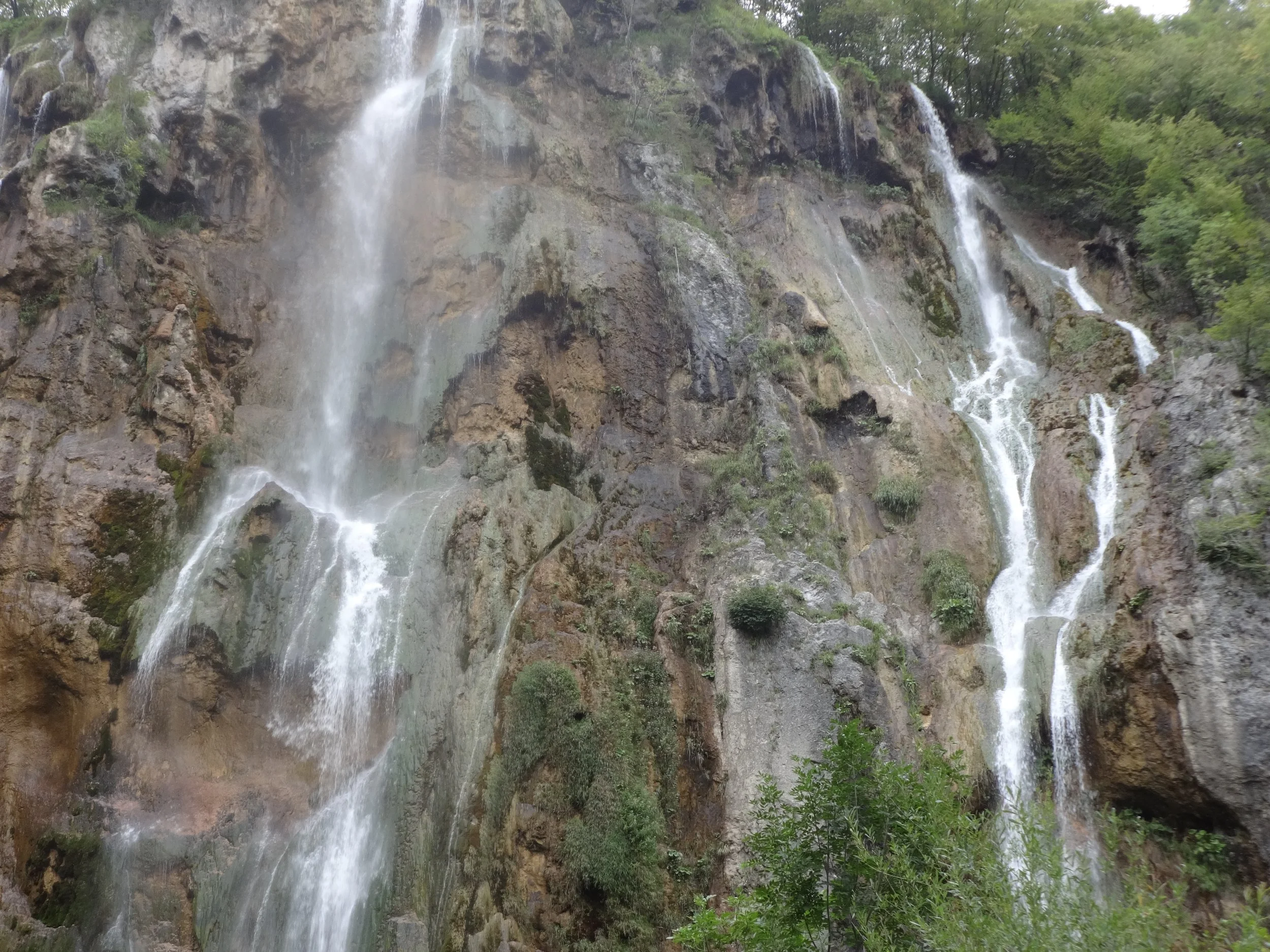 Multiple waterfalls cascading down a rocky cliff surrounded by lush green trees and vegetation.