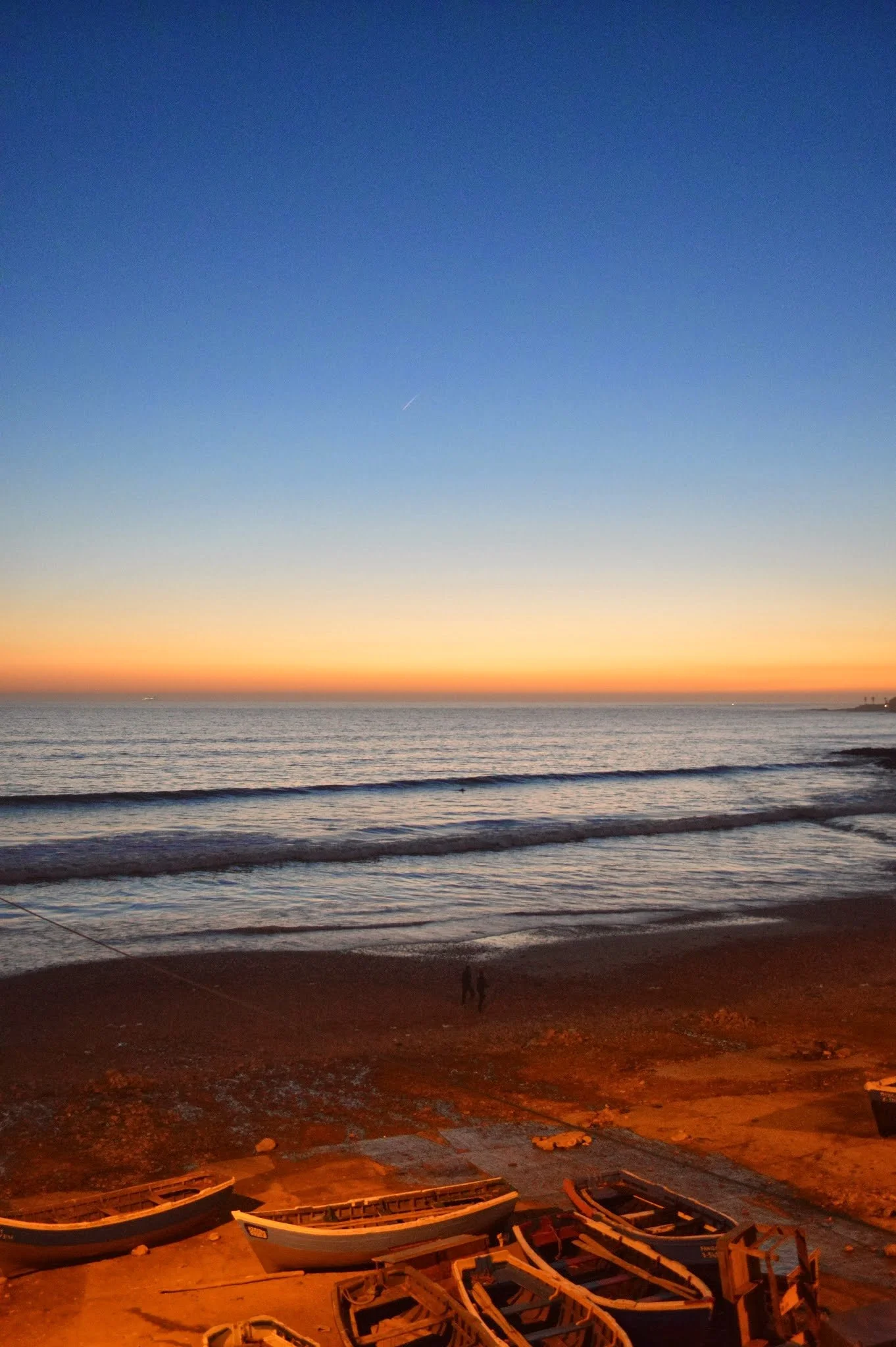 Sunset over the ocean with boats on the sandy beach and a clear sky.